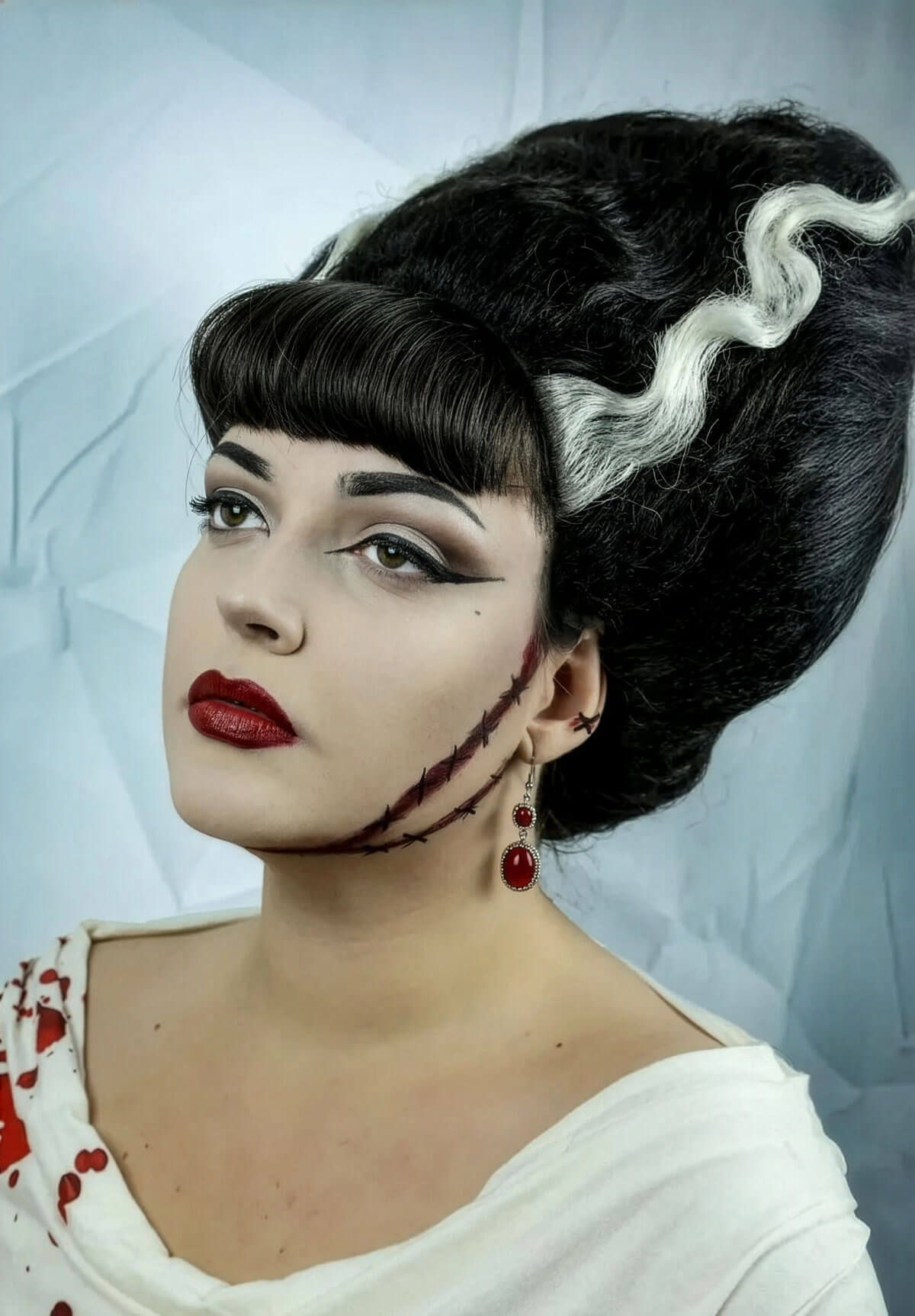 Woman with vintage-style makeup and hair, wearing a white top. Bride of Frankenstein lacefront wig, black with platinum streaks: Eva