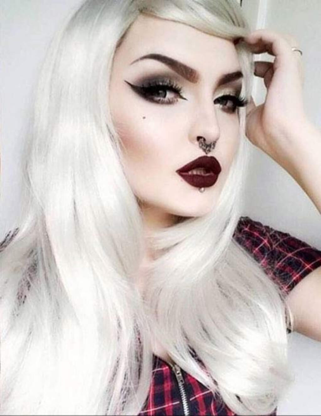 Person with long white hair and dark makeup, wearing a plaid shirt. Long silver/grey wig in razor cut, face framing style: London