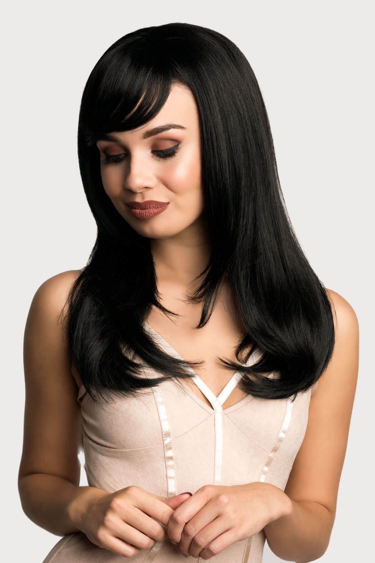 Woman with long black hair wearing a beige top on a light gray background. Long black wig, face frame style with full, sweeping fringe: Corina