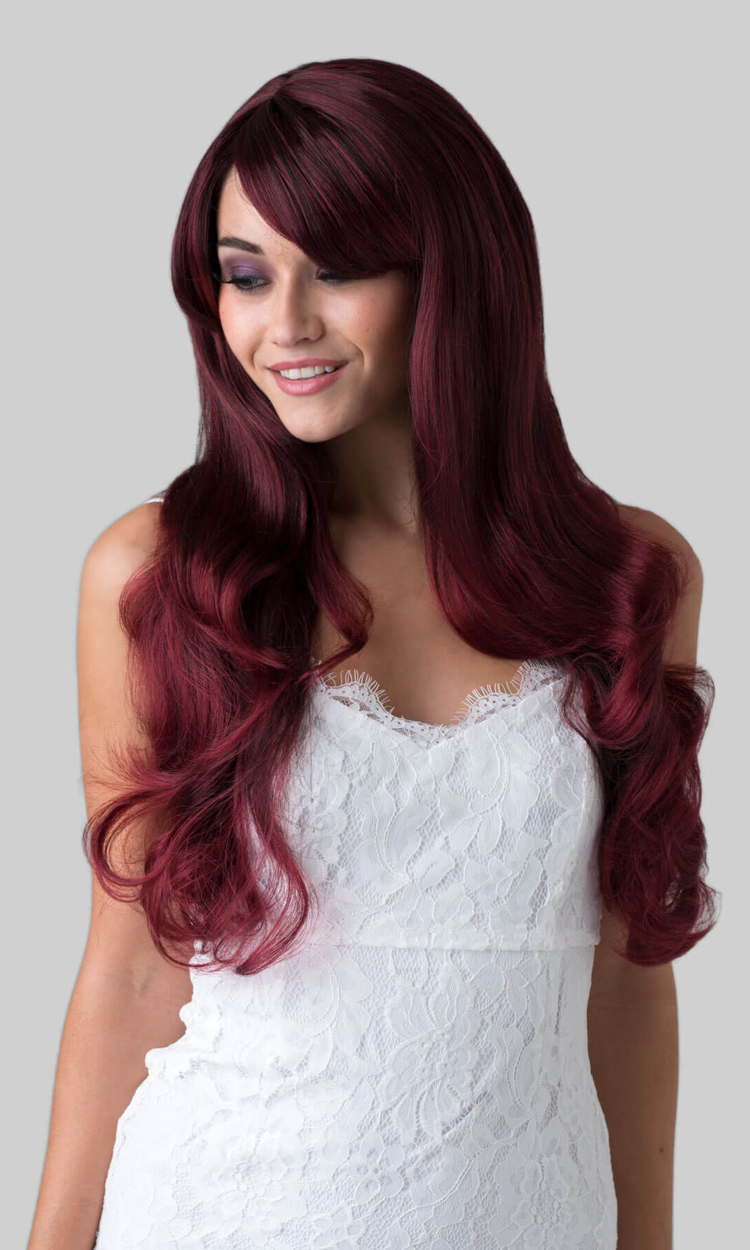 Woman with long burgundy wig wearing a white dress on a grey background. Long red wavy wig with black lowlights: Anji