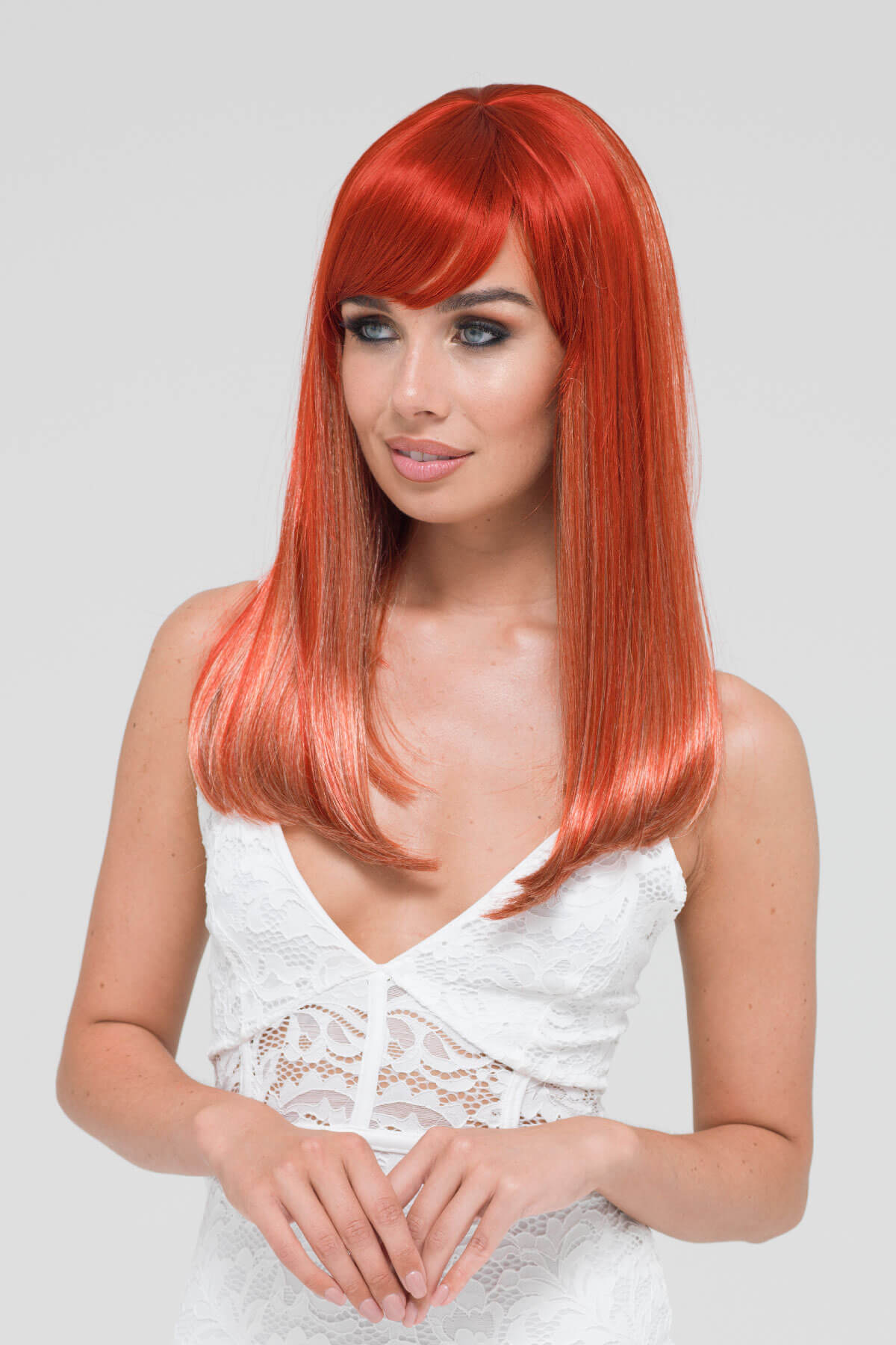 Woman with vibrant red hair wearing a white dress against a light gray background. Copper red and blonde wig with straight fringe: Mathilda