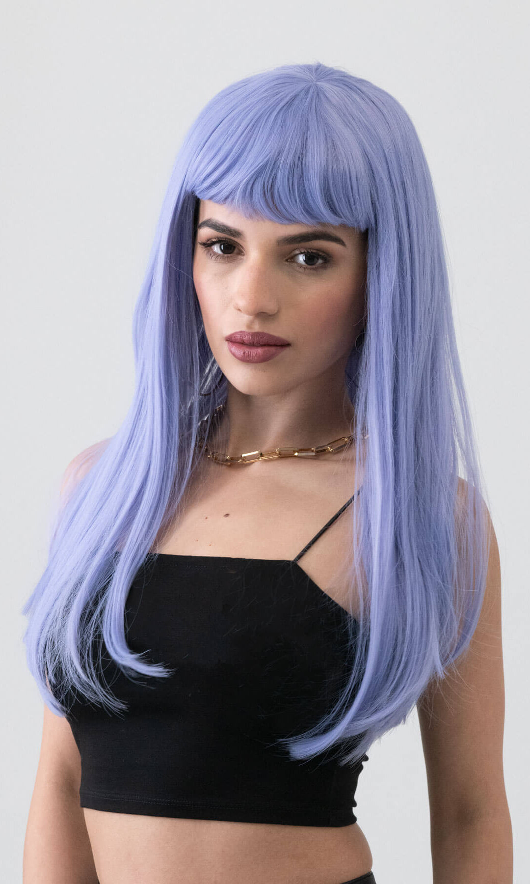 Woman with a lavender wig wearing a black top against a plain background. Long blue wig with short, straight fringe: Alyssa