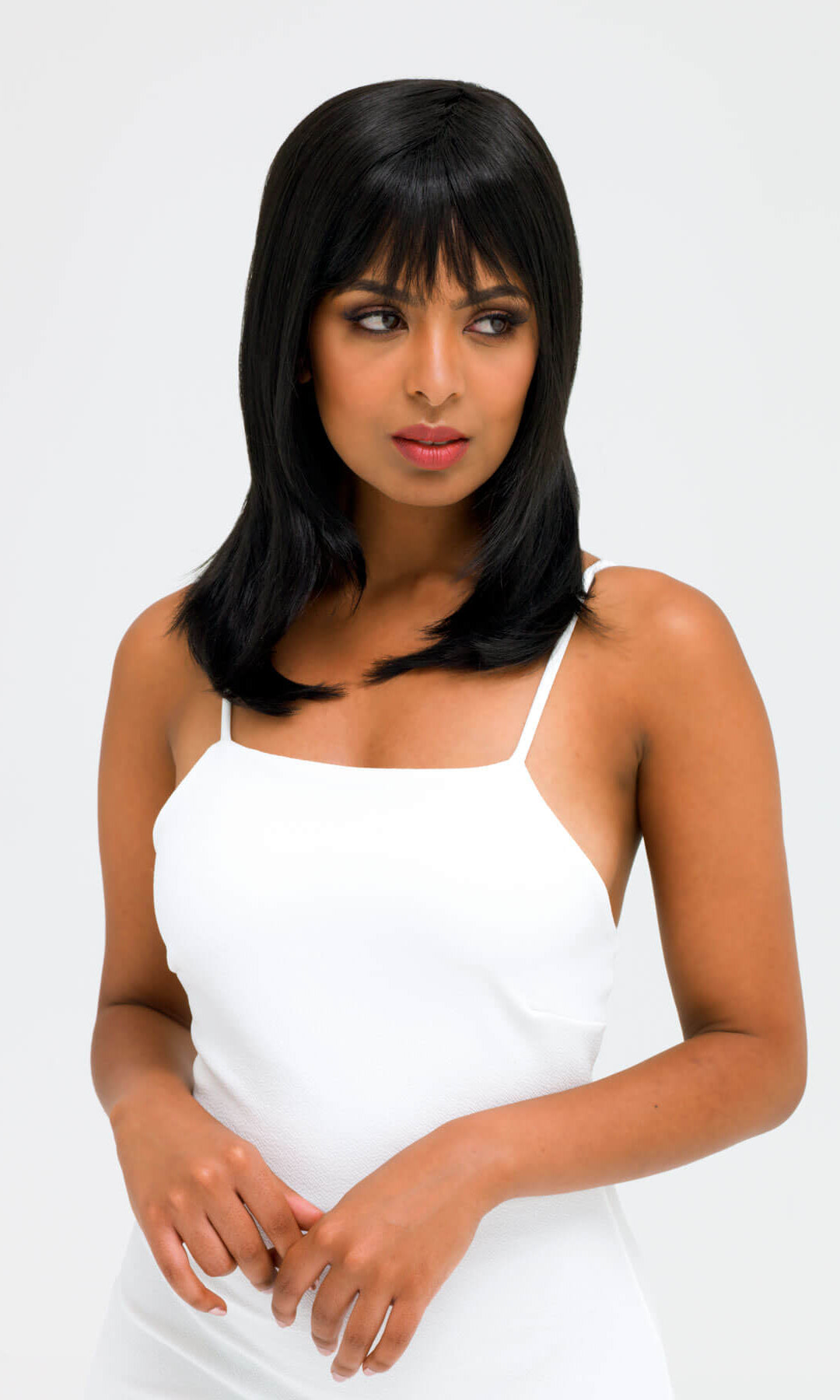Woman wearing a white dress with a plain background. Black wig straight, face frame style: Kristen
