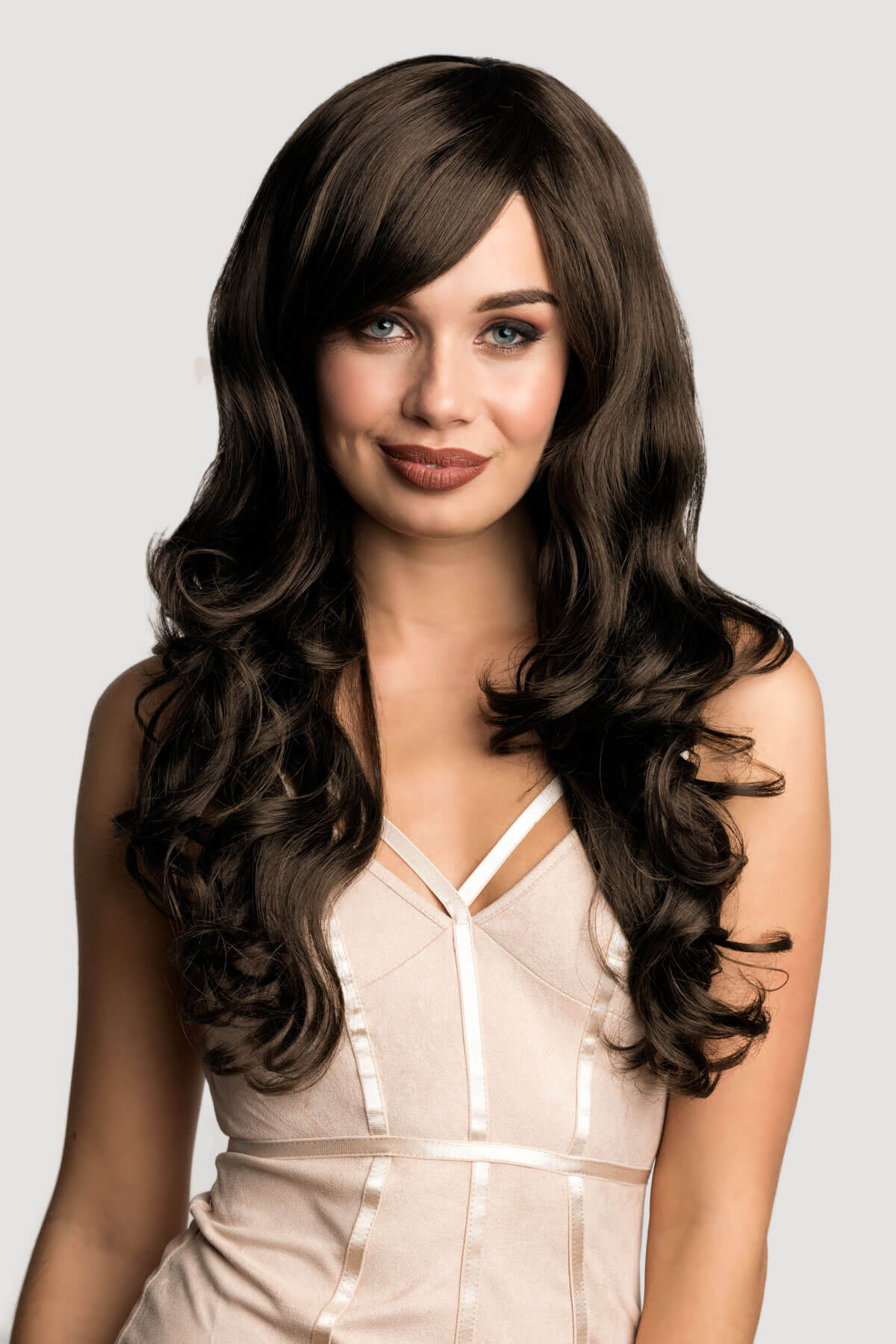 Woman with long, wavy brown hair wearing a beige dress on a light grey background. Long brown wig with gentle waves: Bella chestnut brown 8