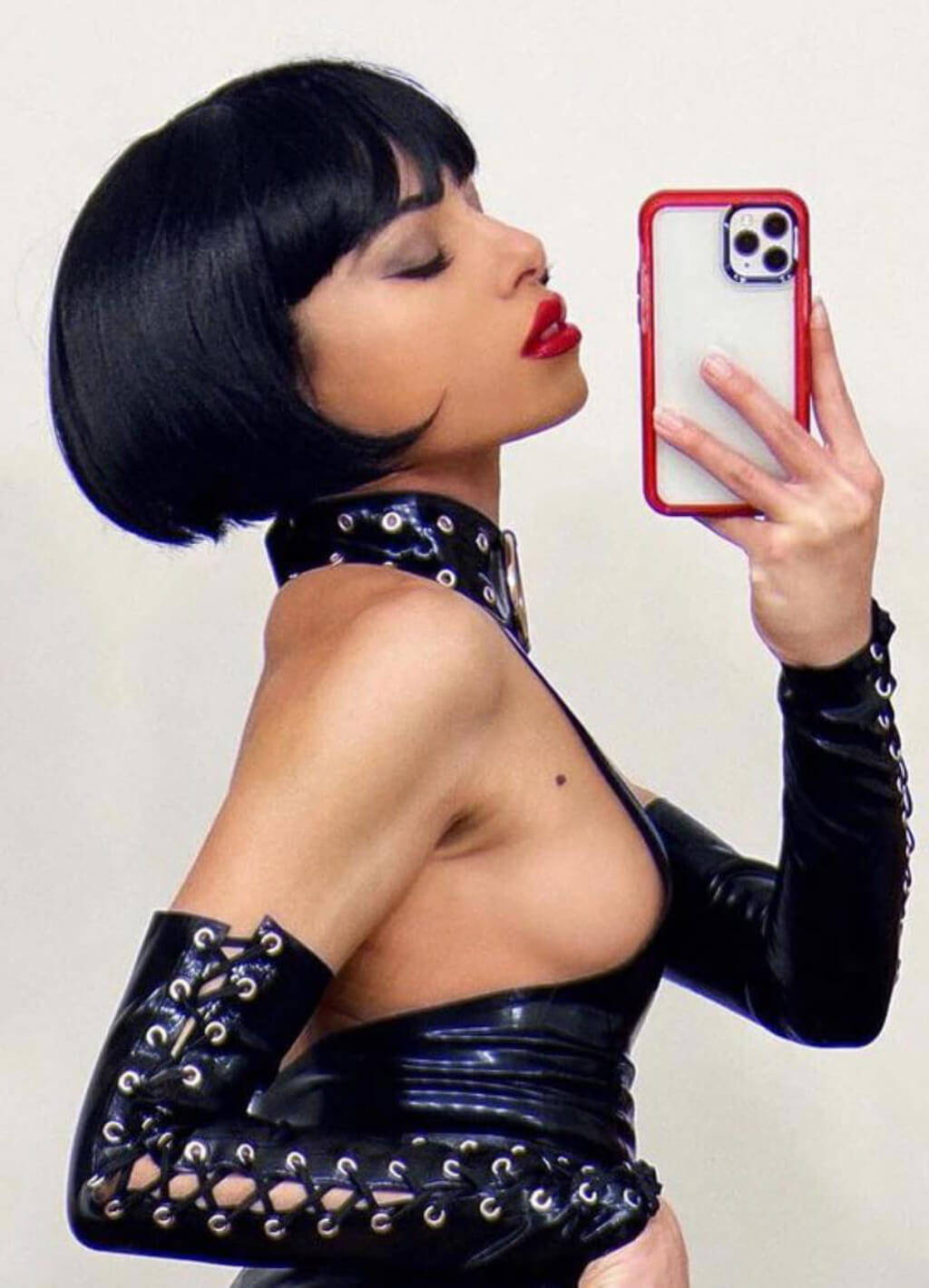 Woman in black outfit taking a selfie with a phone. Louise Brooks style wig, short black bob: Brooks