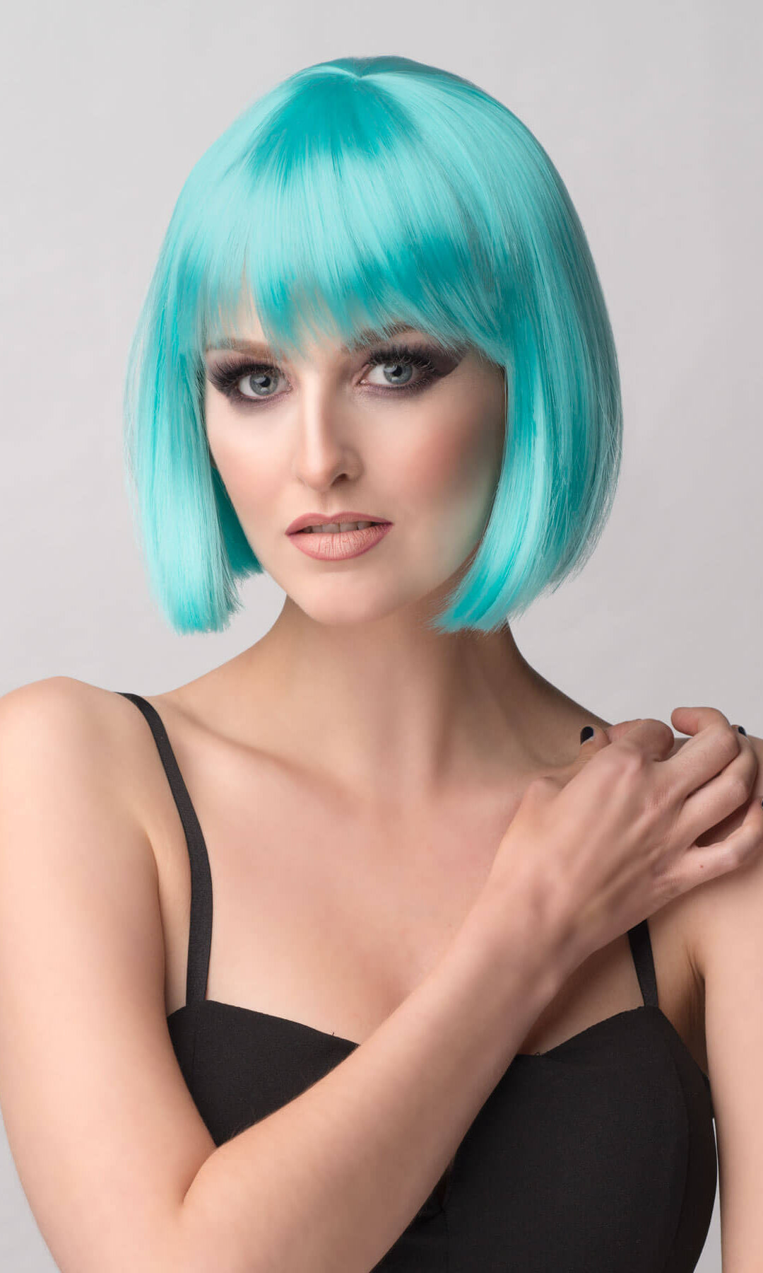 Woman with turquoise hair styled in a bob against a gray background. Turquoise bob wig with full fringe: Iris
