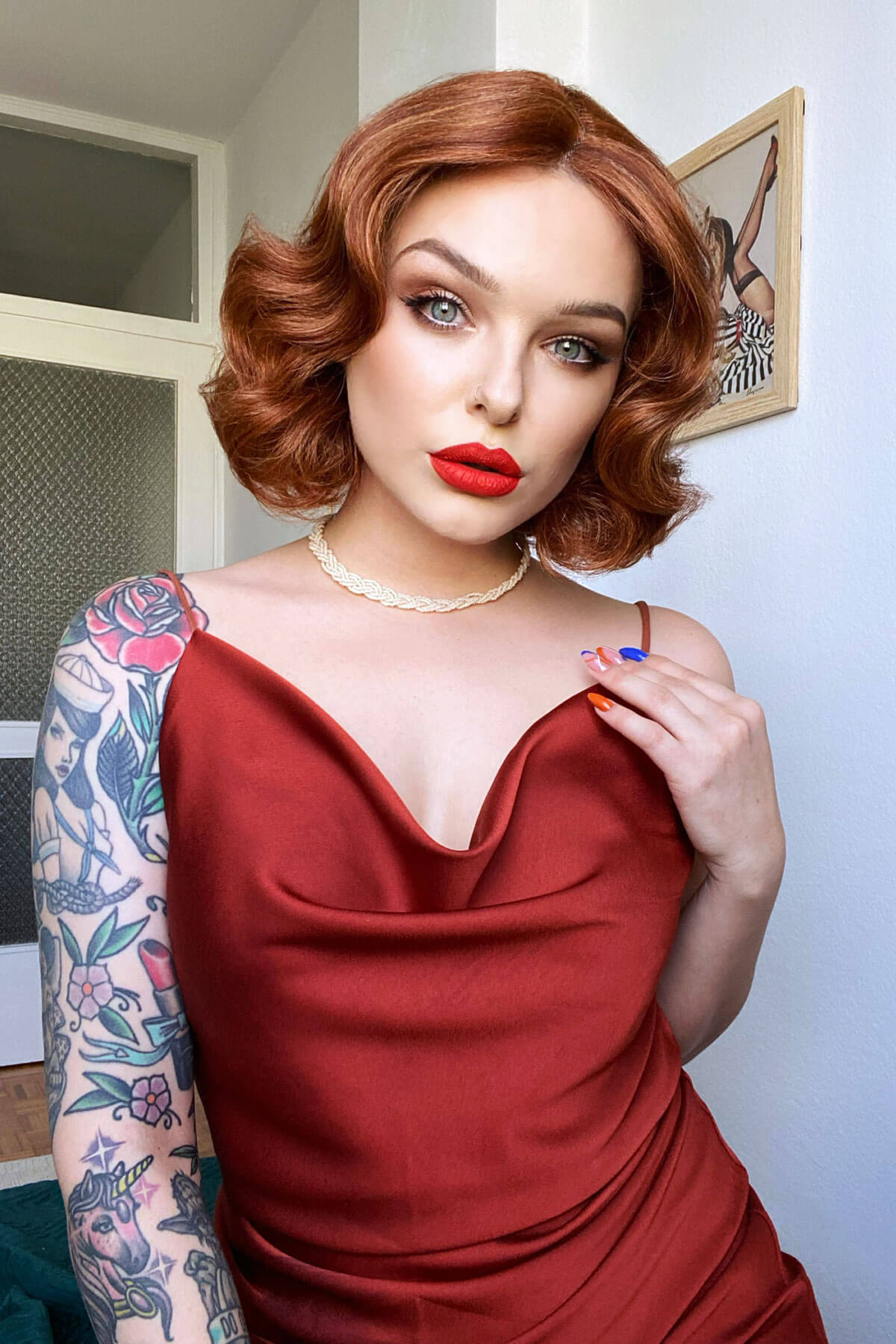 Woman in a red dress with tattoos on her arm, wearing a necklace. Red, auburn & blonde pinup wig, lace front, vintage style: Ginny