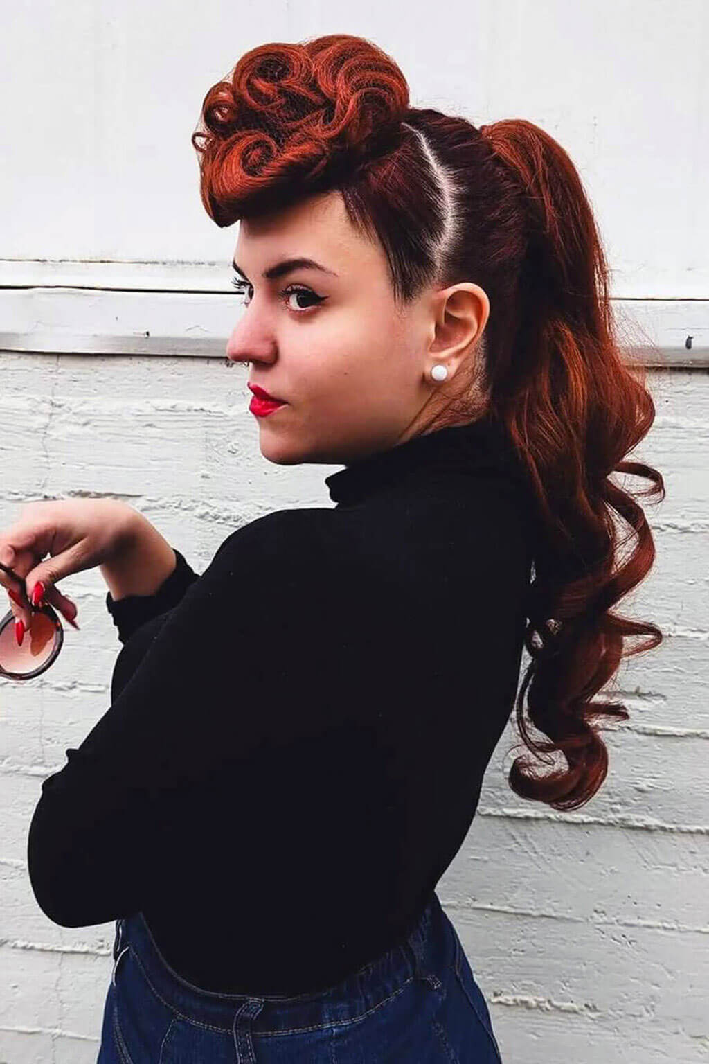 Woman with styled red hair against a white brick wall. Woman with styled red hair in a ponytail against a white wall. Hair poodle clip-in hairpiece bun vintage style 1950s: Lucille copper red 130