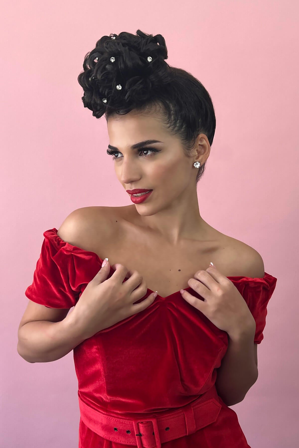 Woman wearing a red off-shoulder dress with a pink background. Hair poodle clip-in hairpiece bun vintage style 1950s: Lucille jet black 1