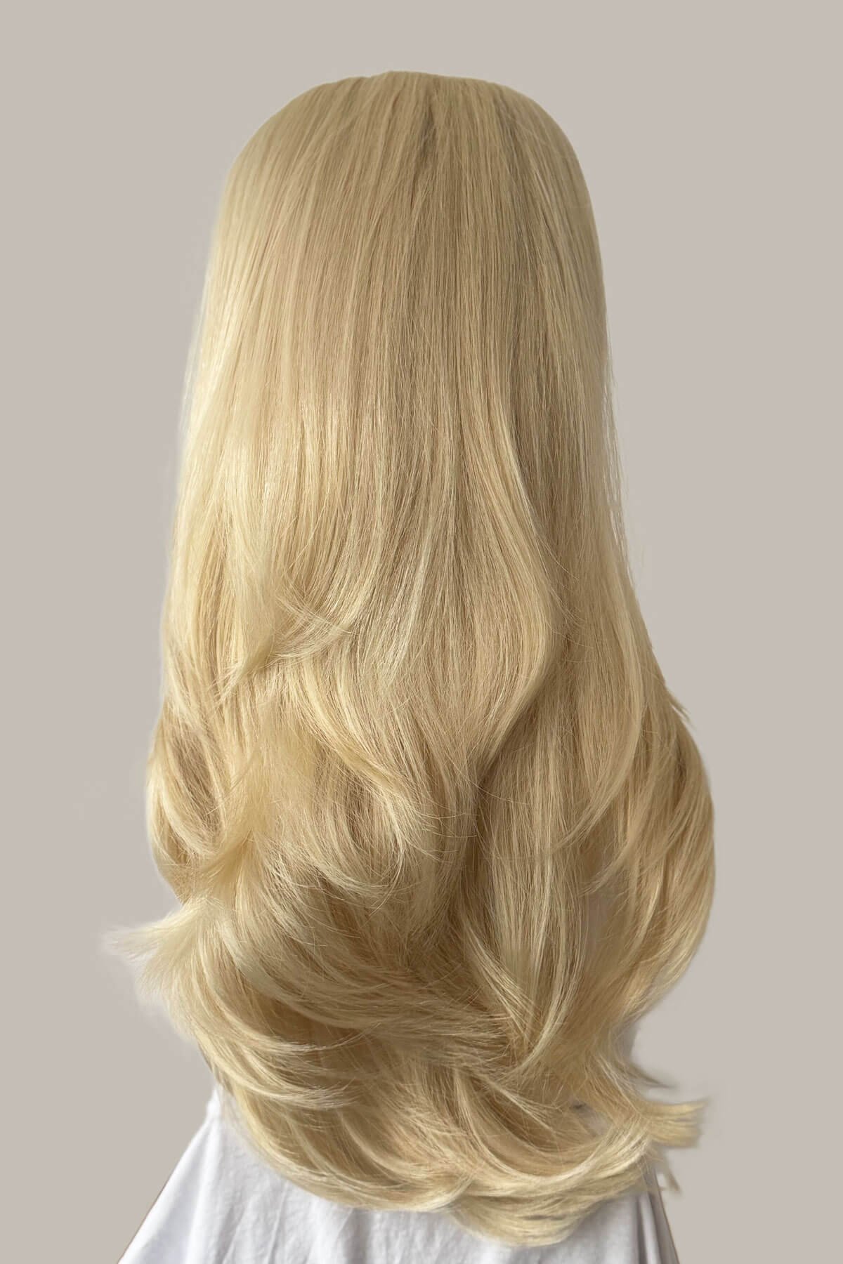 Blonde wig on a mannequin head against a neutral background.  1960s style hair, high crown long straight and layered half wig: Juliette champagne blonde 613