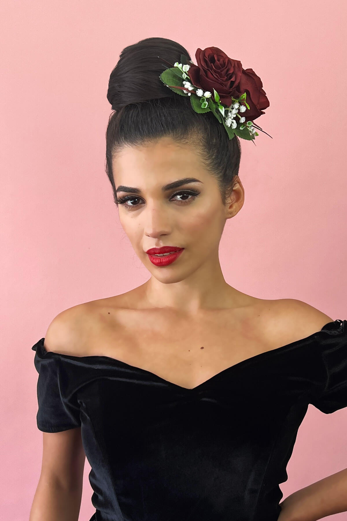 Woman wearing a black velvet off-shoulder top with floral headpiece against a pink background. Hairpiece bun; instant perfect bun hairpiece: Hepburn