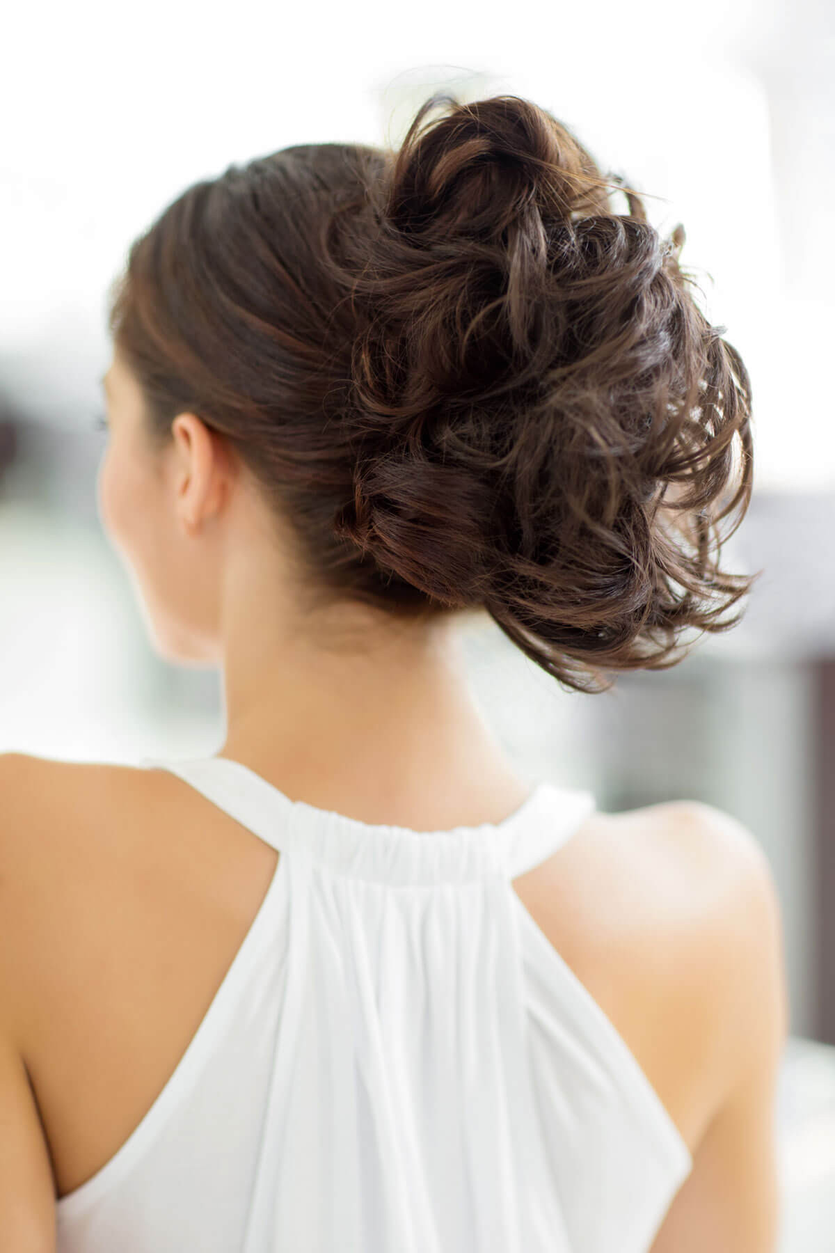 Woman with an elegant updo hairstyle wearing a white dress against a blurred background. Clip in hairpiece, ponytail, short, flexihair: Leela chestnut brown 8