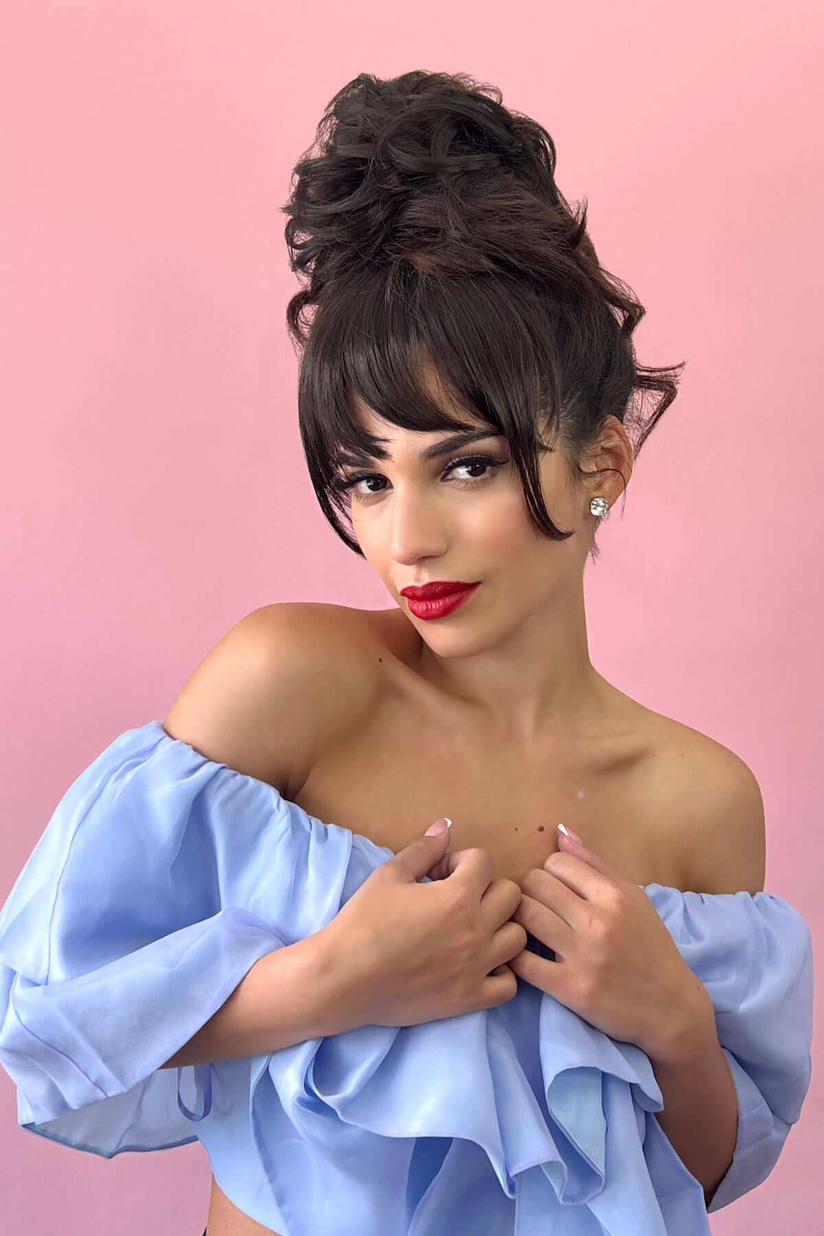 Woman with styled hair and red lipstick wearing a light blue off-shoulder top against a pink background. Scrunchie bun hairpiece, easy updo messy bun: Betsy dark brown 4