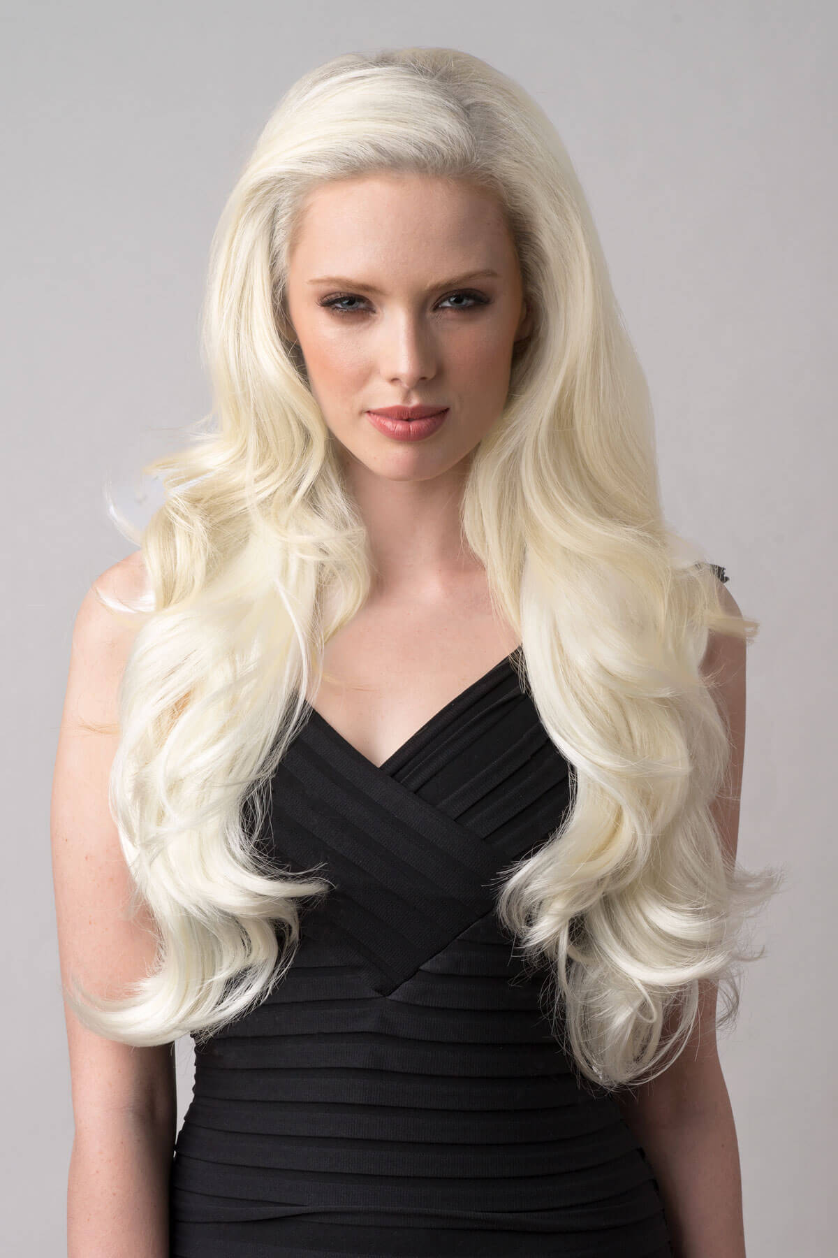 Woman with long blonde wig wearing a black dress against a gray background. Platinum blonde half wig hairpiece (3/4 wig), wavy: Barbie