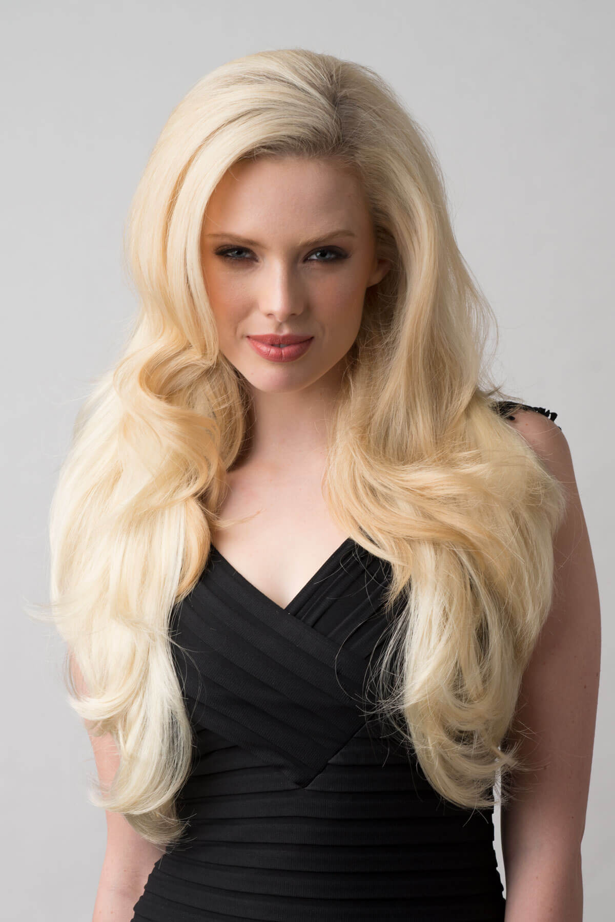 Woman with long blonde hair wearing a black dress against a gray background. Long blonde half wig hairpiece (3/4 wig) loose curls: Frankii creamy blonde 613