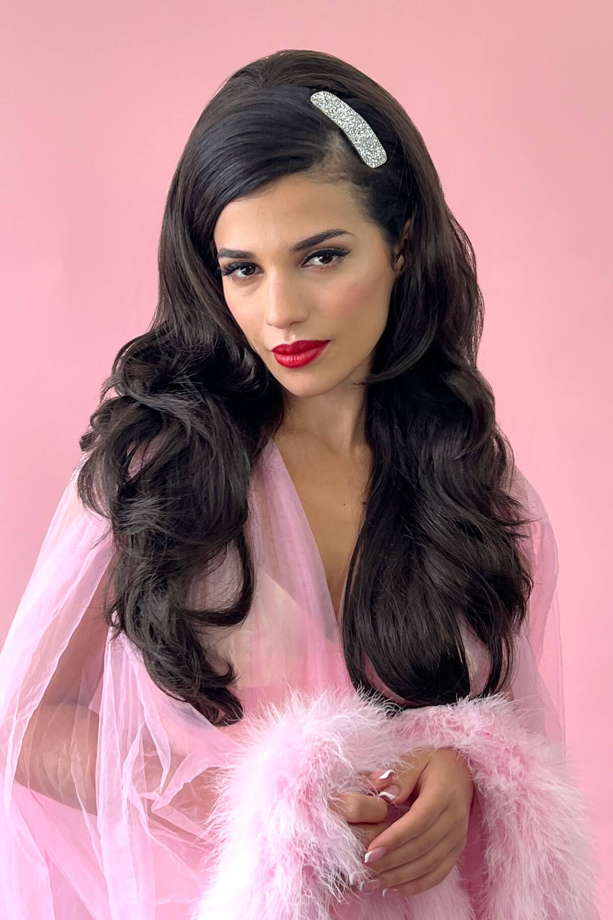 Woman with long dark hair and red lipstick wearing a pink dress against a pink background. 8H27 