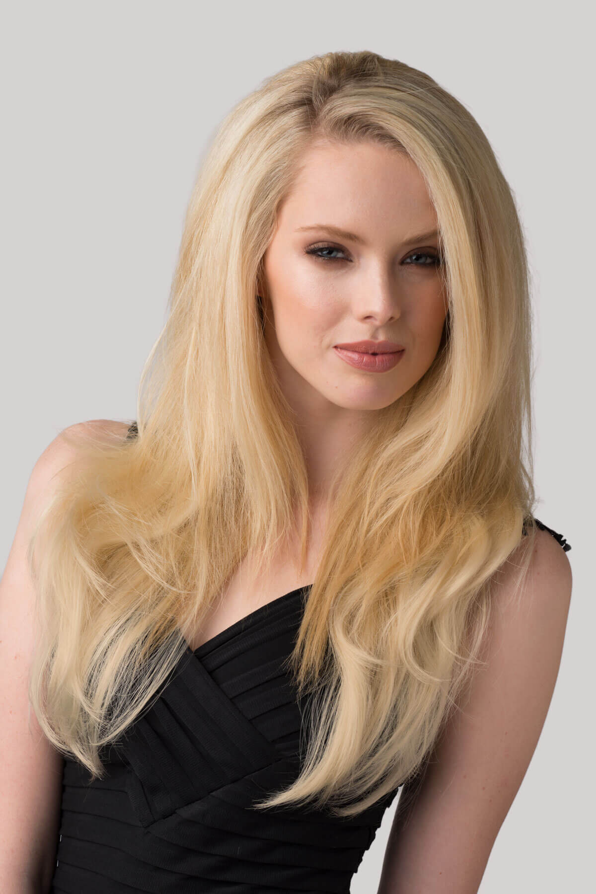 Woman with long blonde hair wearing a black dress against a gray background.  Straight blonde half wig hairpiece (3/4 wig), layered: Autumn blonde 24BT613