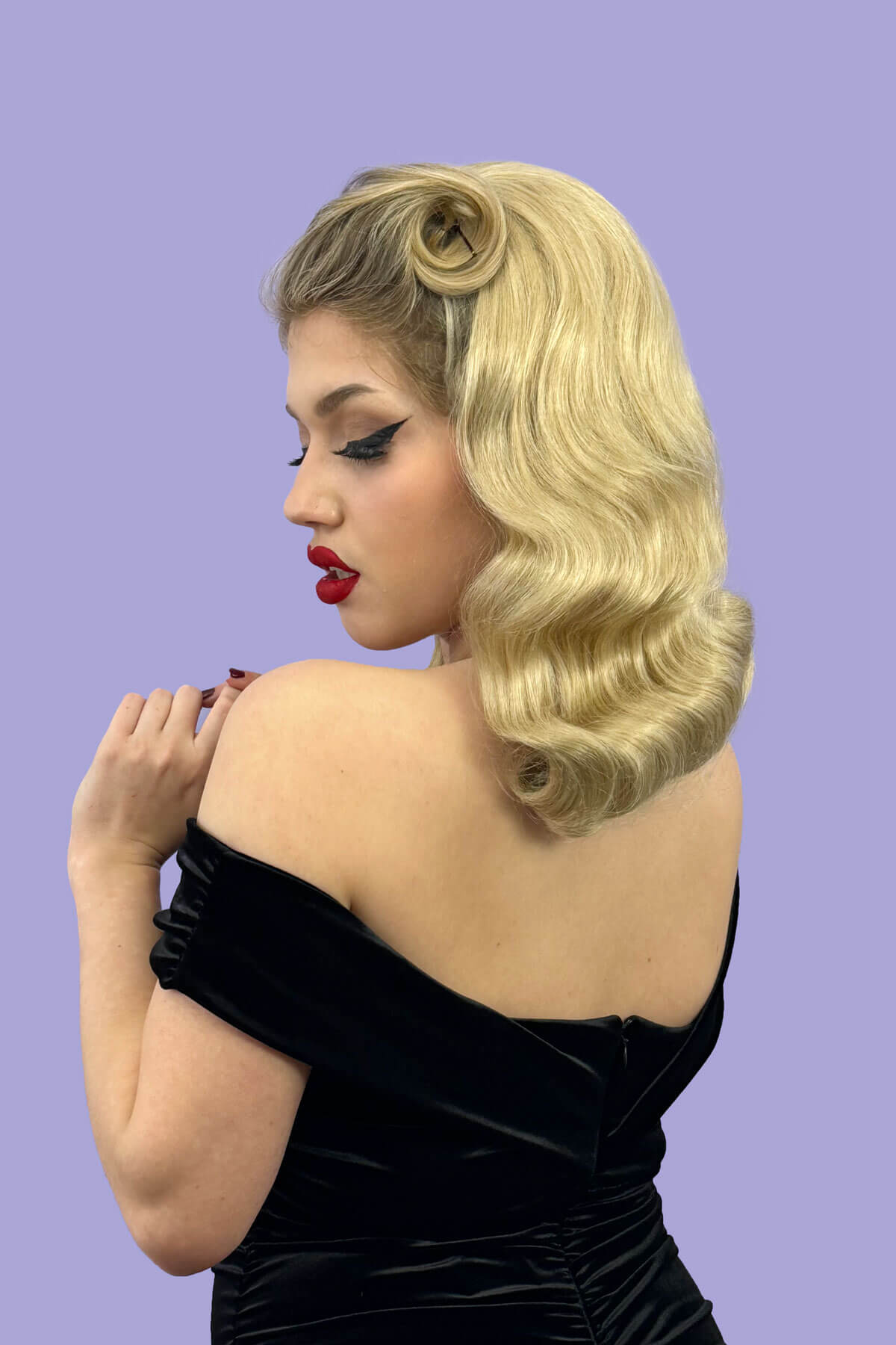 Woman with vintage-style blonde hair and red lipstick wearing a black dress against a purple background. 1950s style half wig hairpiece with deep finger waves: Deborah blonde 613T24