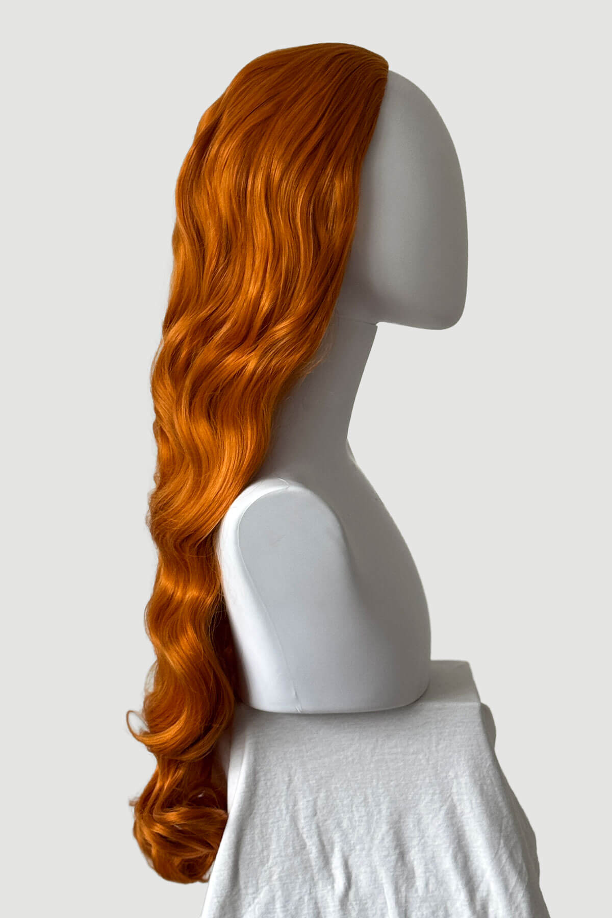 Mannequin head with long, ginger hair styled in a ponytail on a plain background. Ultra long half wig with hollywood waves. ginger
