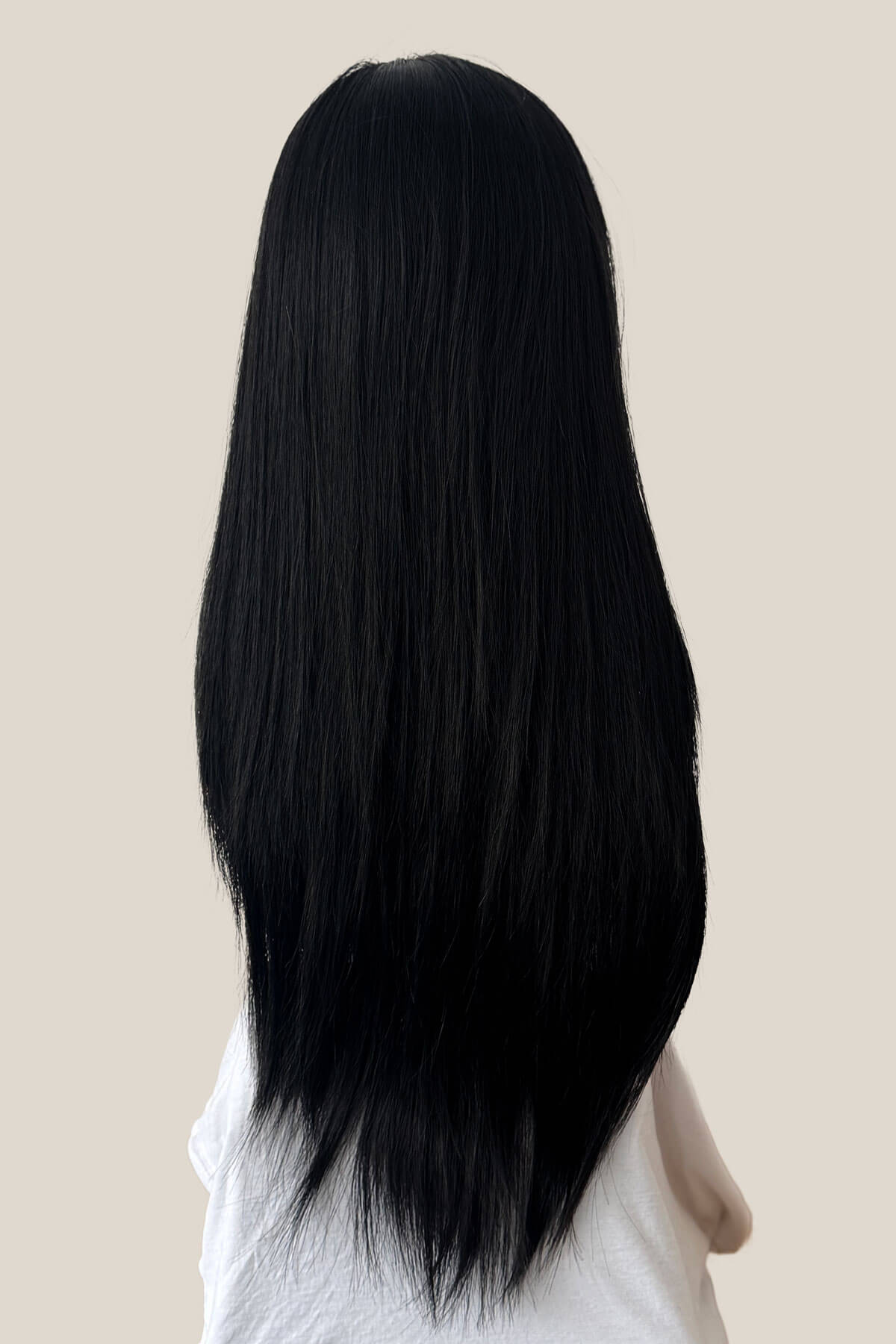Person with long black hair on a beige background. Straight black half wig hairpiece extension (3/4 wig): Theda black 1B