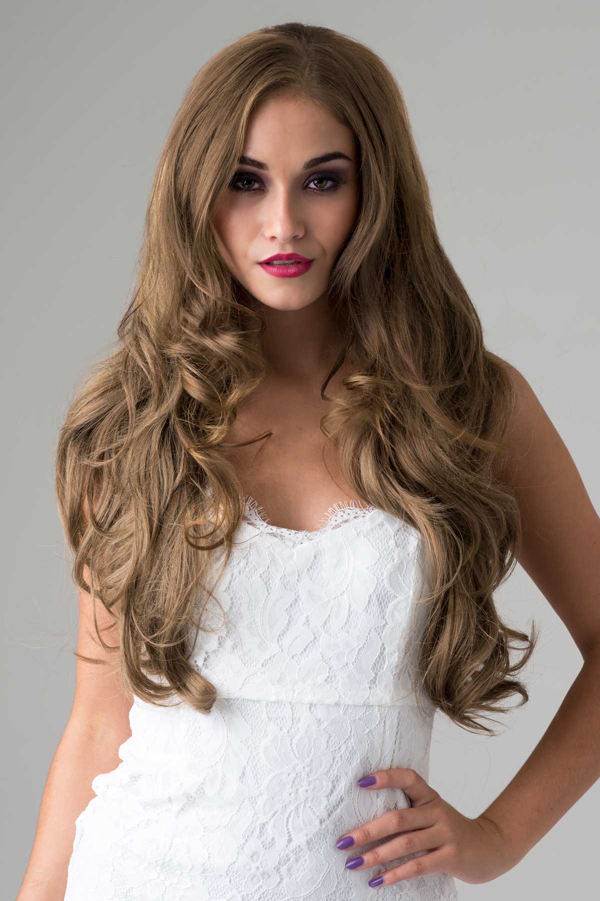 Woman with long, wavy brown hair wearing a white dress against a gray background. Light golden brown half wig hairpiece, wavy: Teresa