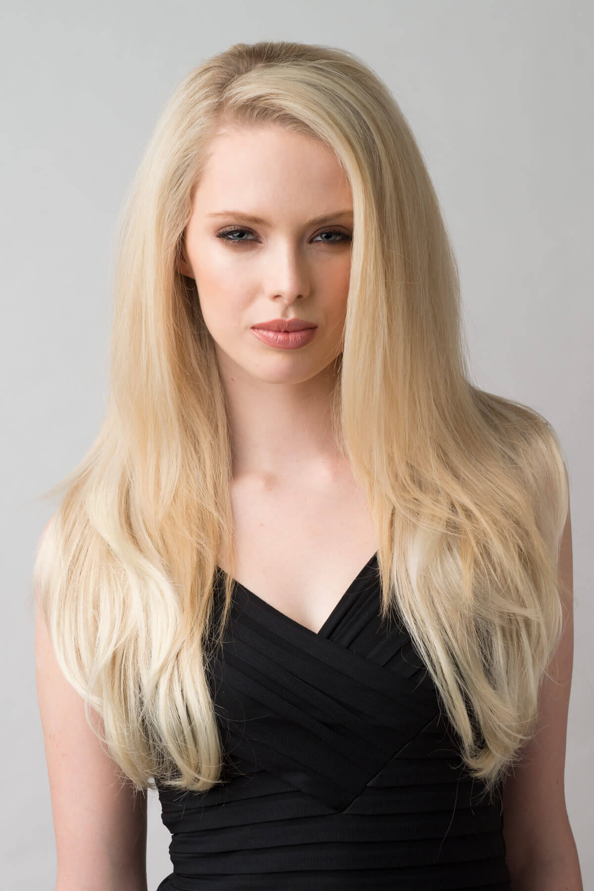 Woman with long blonde hair wearing a black dress against a gray background. Straight blonde half wig hairpiece (3/4 wig), layered: Autumn ash blonde to light blonde 613T24