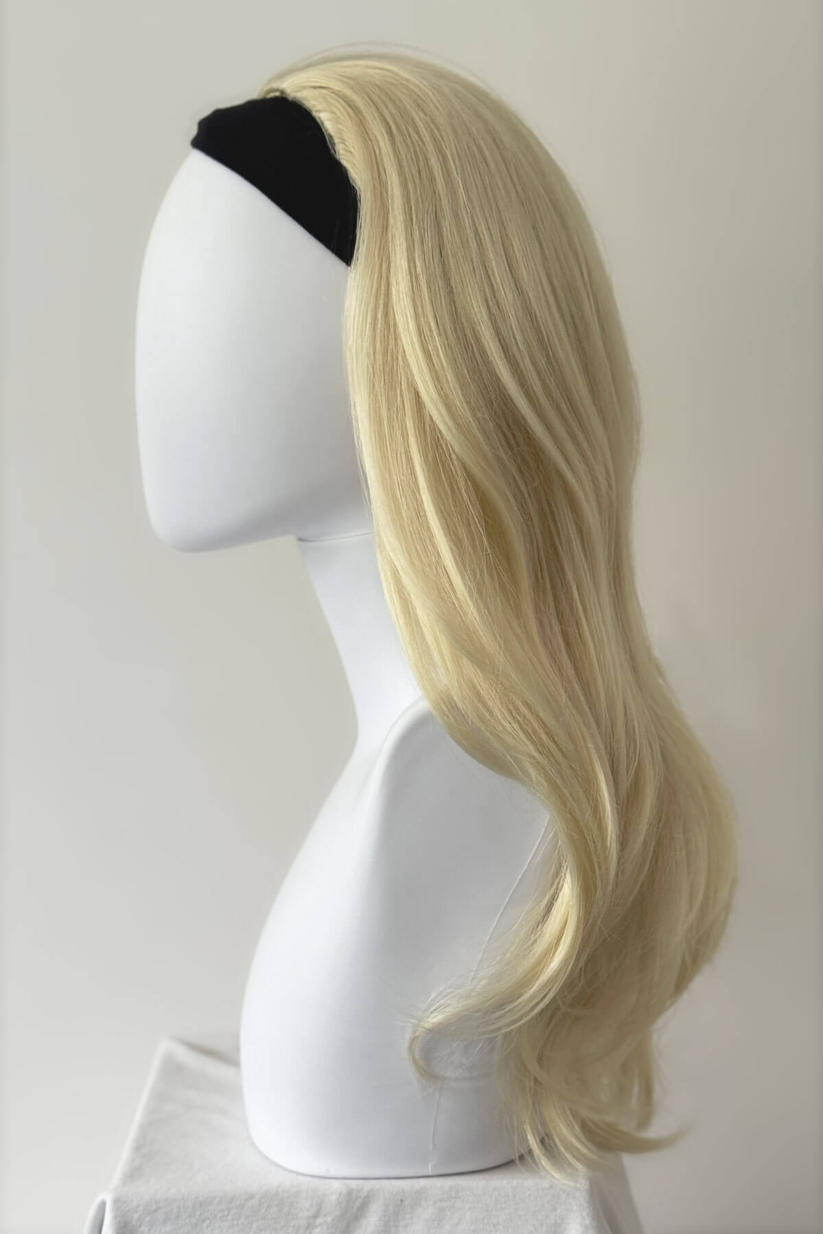 Blonde wig on a mannequin head against a plain background. Blonde half wig hairpiece (3/4 wig), gently layered: Sabrine champagne blonde 613