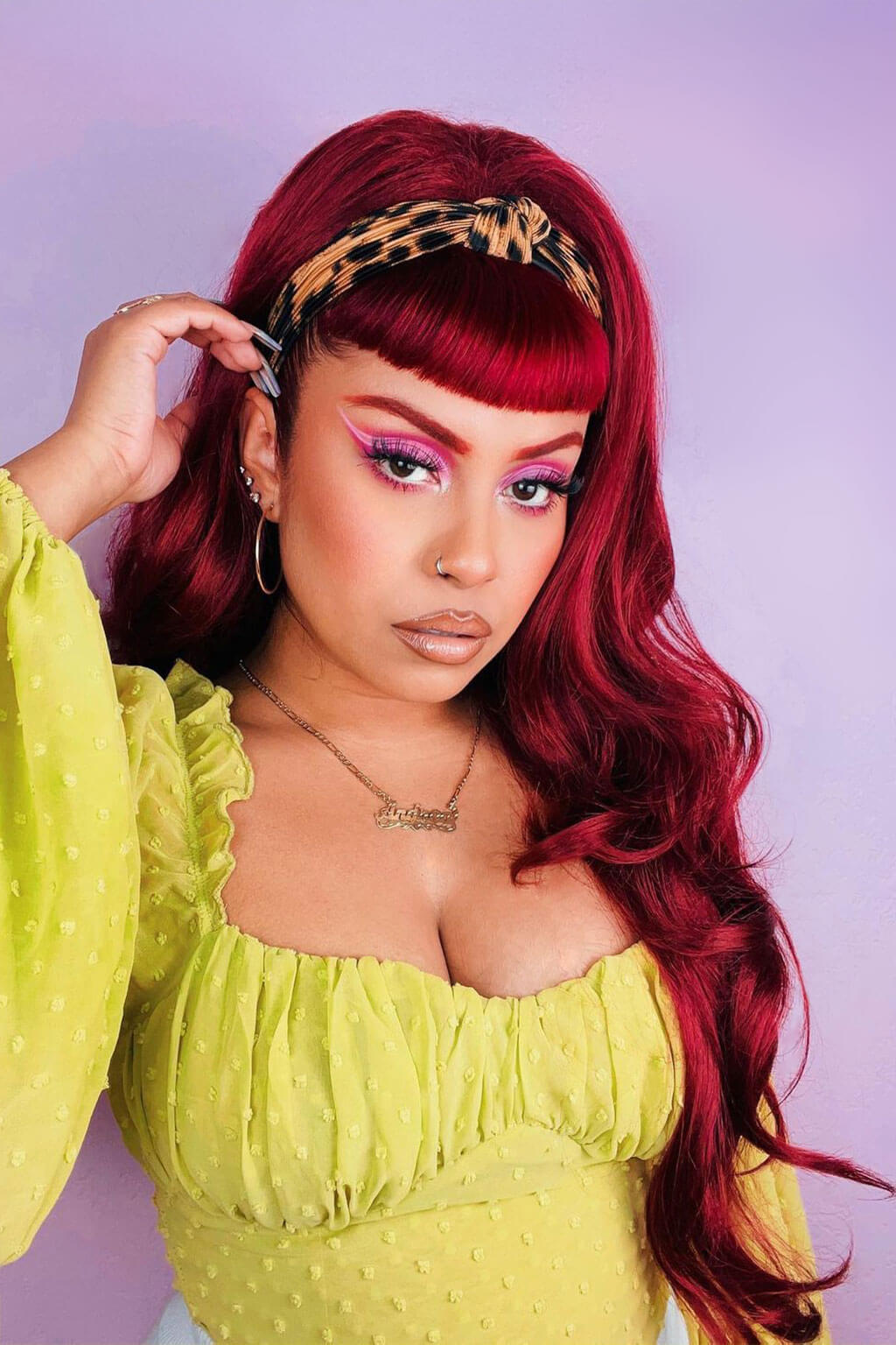 Woman with vibrant red hair and colorful makeup wearing a yellow top against a light purple background - High crown long, wavy half wig and volume ring, cherry red: Bardot 39