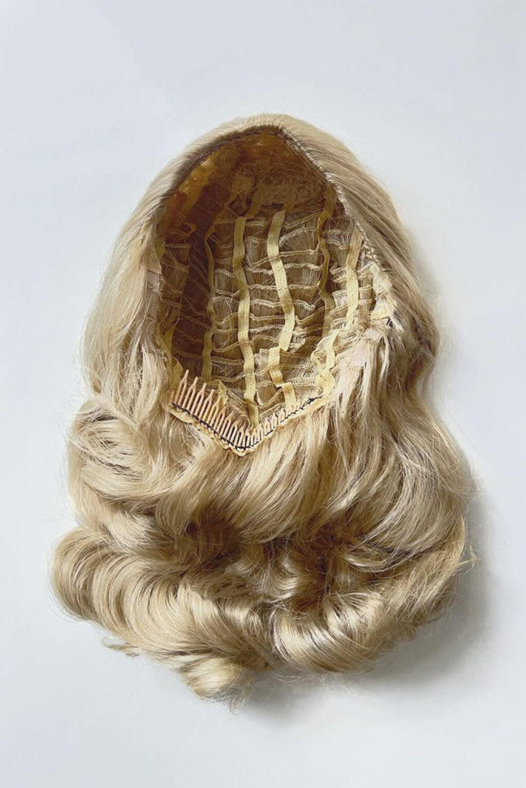 Blonde hairpiece with a comb on a white background. 1950s style half wig hairpiece with beautiful waves: Morgana blonde 613T24