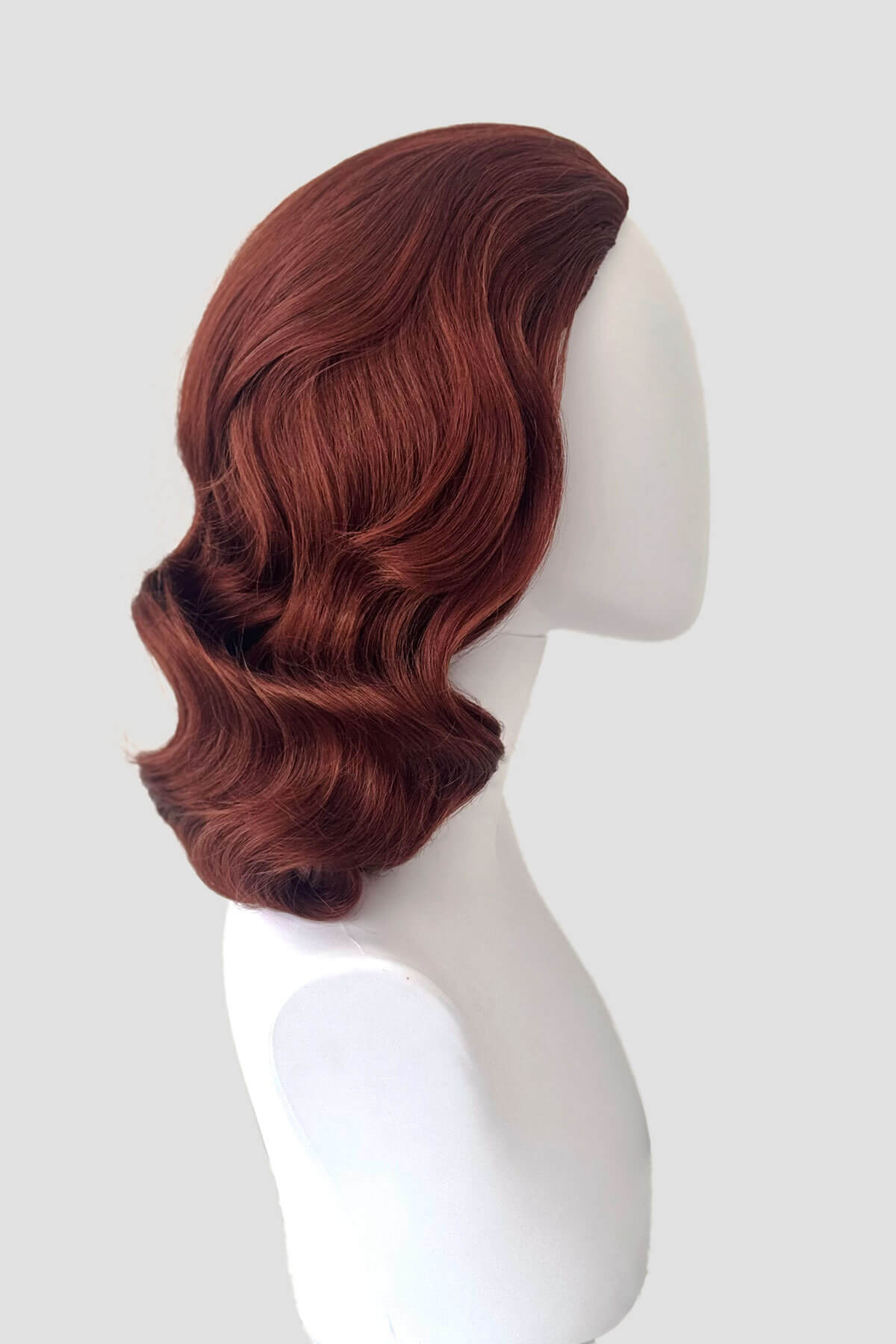 Reddish-brown wig on a white mannequin head against a light gray background. 1940s style half wig hairpiece with beautiful marcel waves: Virginia copper red 130