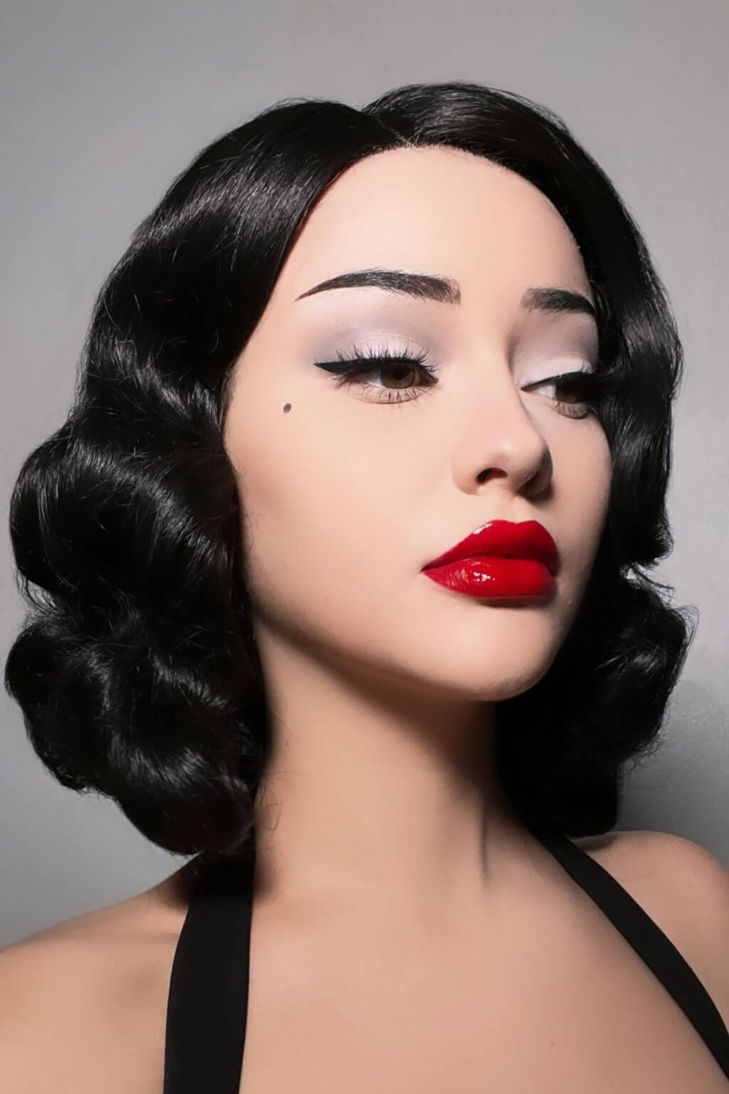 Woman with vintage-style makeup and hair against a gray background. Black lacefront wig, pinup/vintage style, mid length with finger waves: Etta