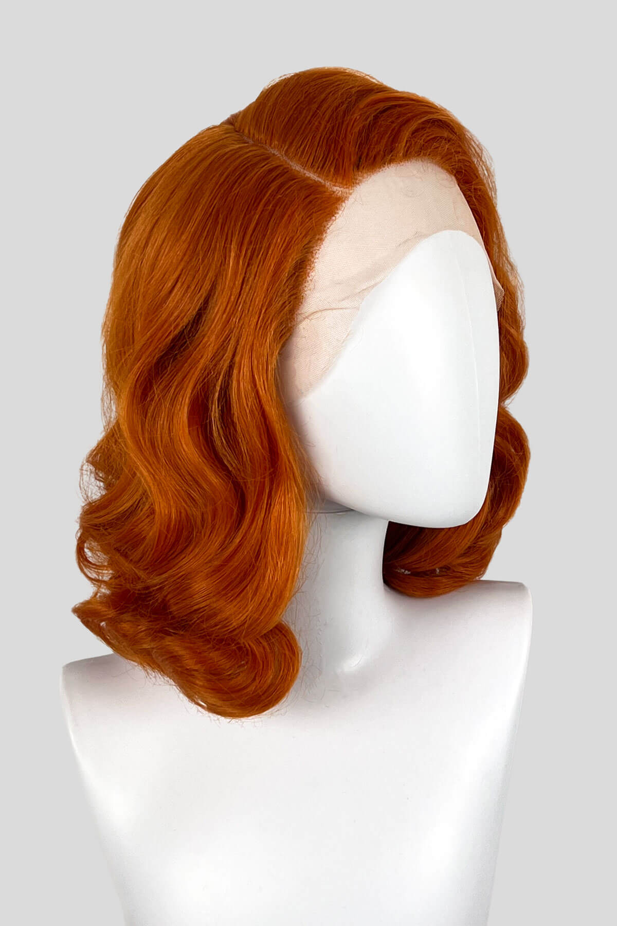 Reddish-brown wig on a white mannequin head against a white background. Ginger lace front wig, pinup/vintage style, mid length with finger waves: Flora 