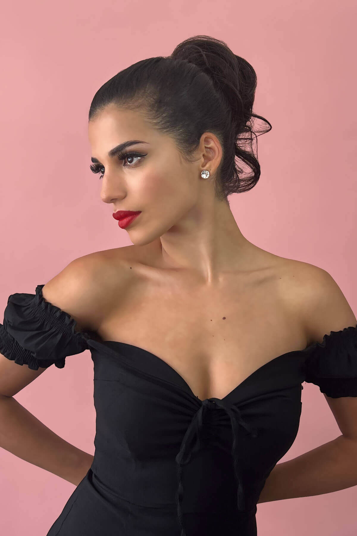 Woman in a black off-shoulder dress with red lipstick against a pink background. Short ponytail extension hairpiece, short with whisps: Leah black 1B