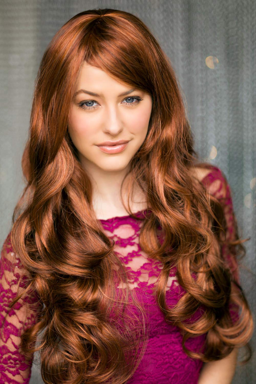 A person wearing a red and auburn wig with blonde highlights, featuring long bouncing curls and waves with a side sweeping fringe. Red & auburn wig with blonde highlights, long: Freya