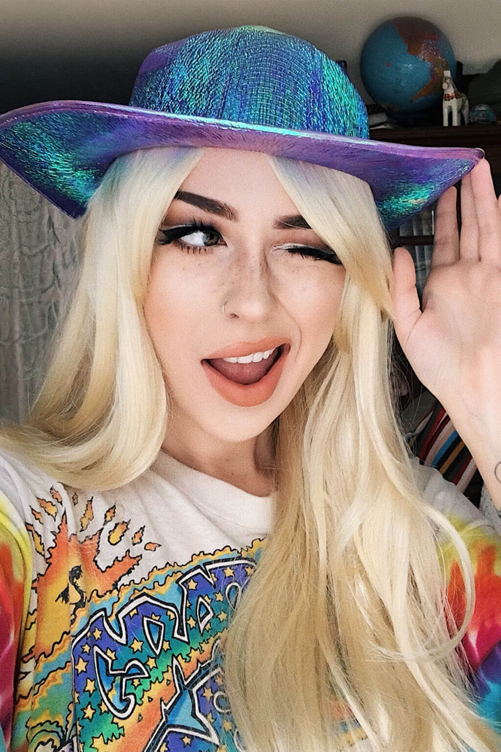Person wearing a colorful hat and a graphic t-shirt with a vibrant design. Long straight blonde wig with no fringe: Juste