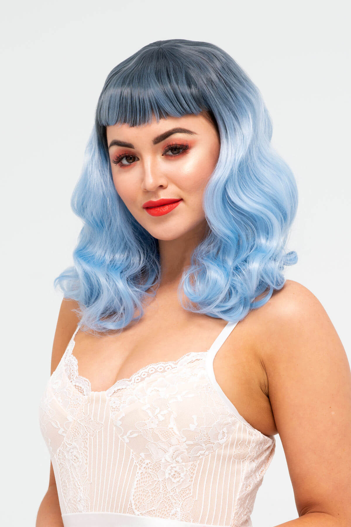 Woman with blue wig and red lipstick on a white background. Black and blue pinup style wig, curled with short fringe, 1950s style: Luna