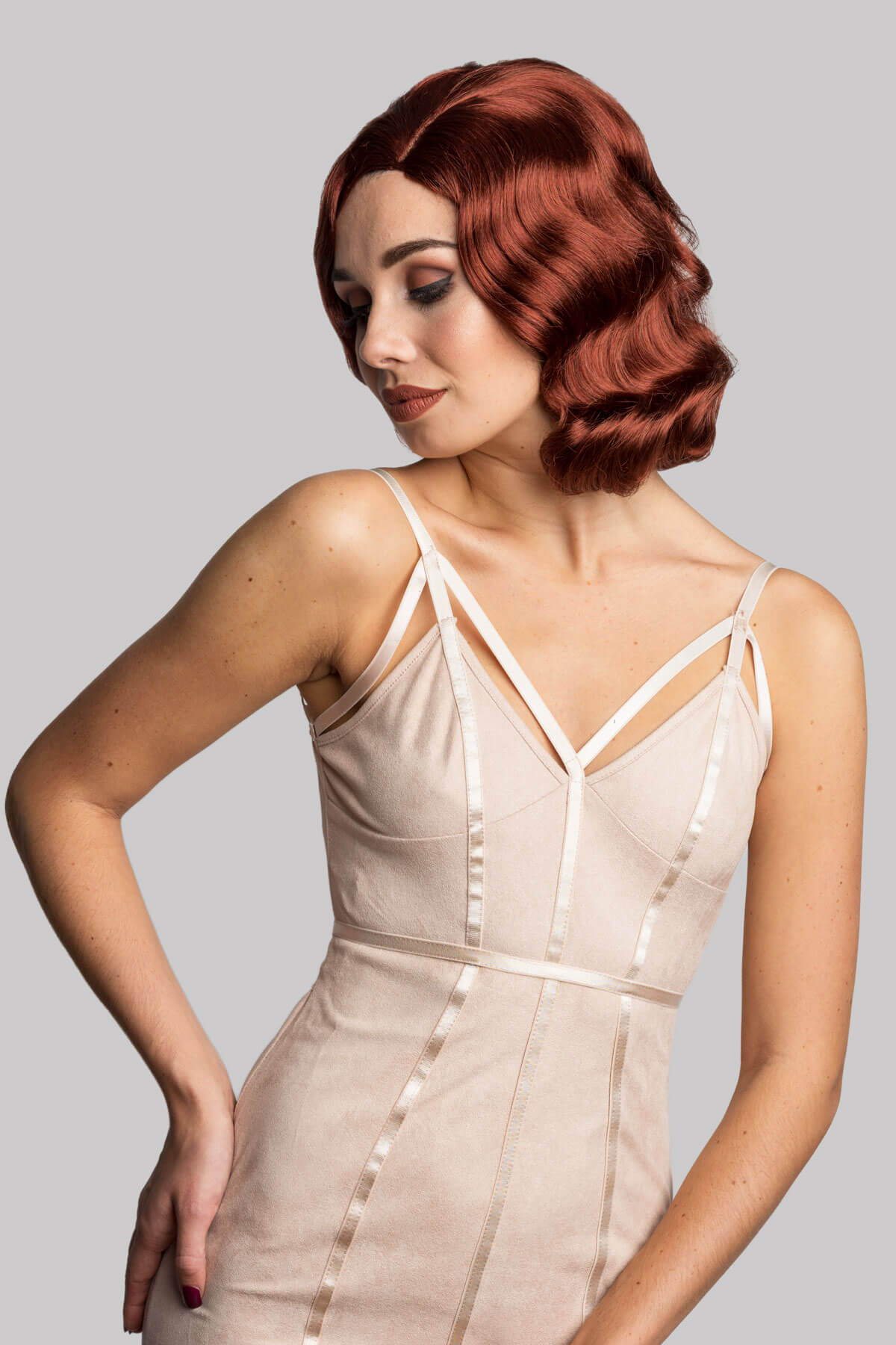 Woman wearing a beige dress with thin straps against a gray background. Copper red 40s style wig with finger waves: Banbury
