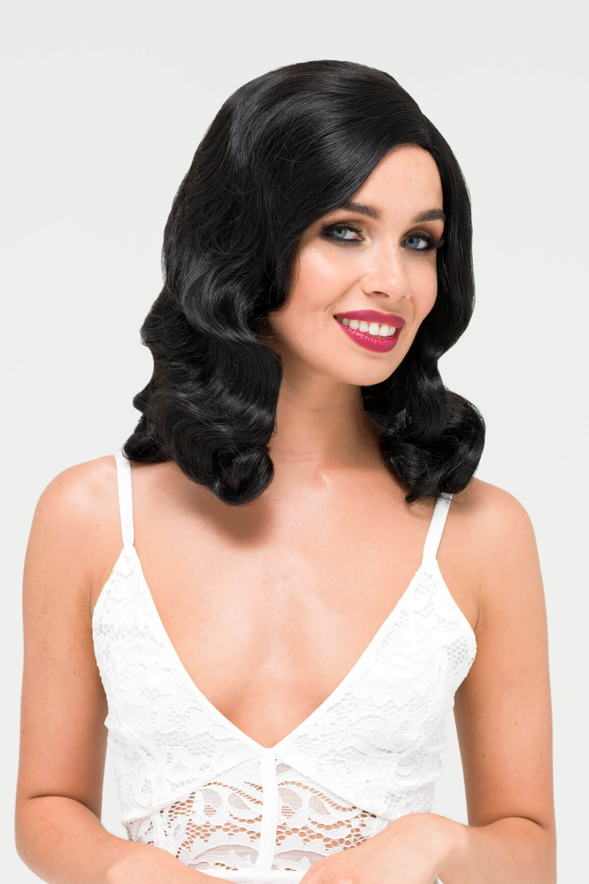 Woman with styled black hair wearing a white lace top on a light gray.background. Black 1930s style wig with long marcel waves: Vivienne