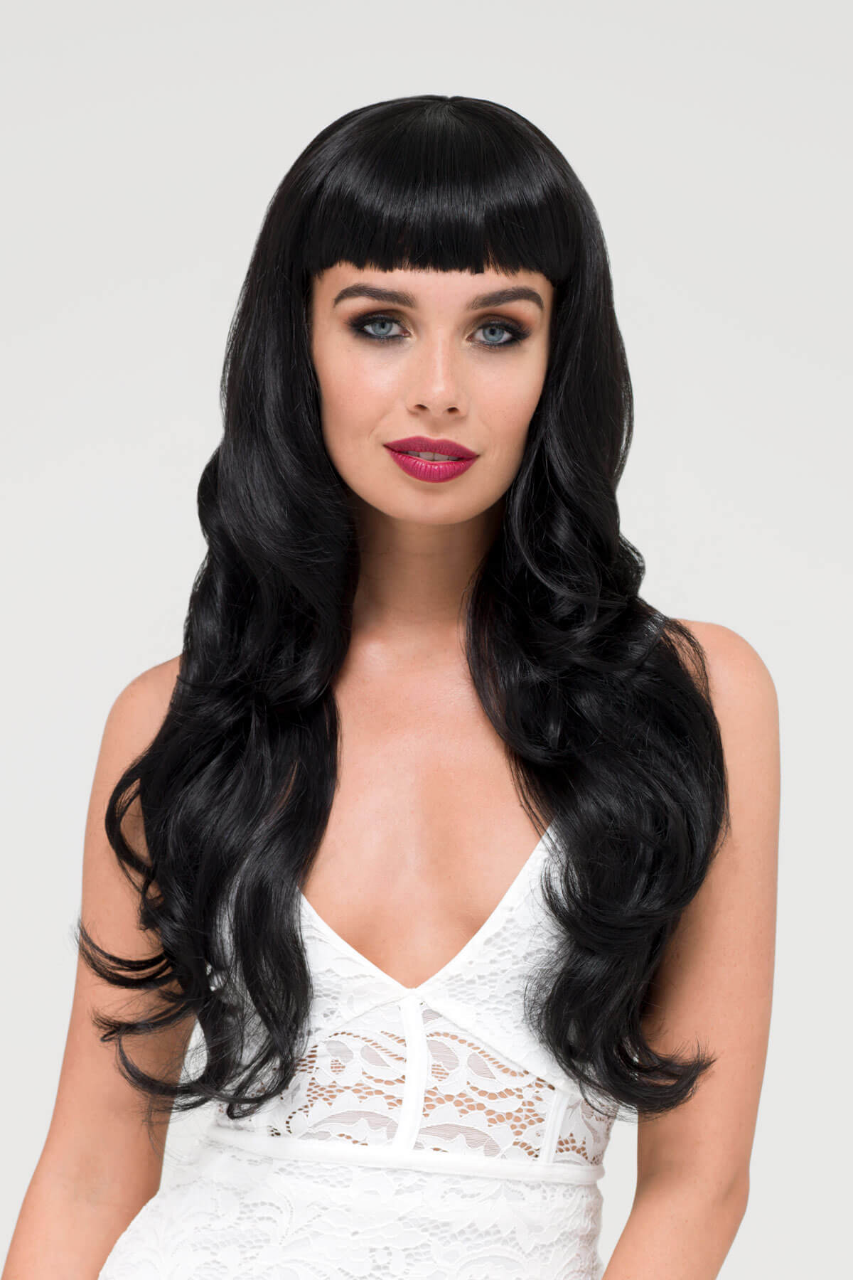 Woman with long black wig and white lace top on a light gray background. Long wavy black wig with vintage-style, rockabilly, straight fringe: Eloise