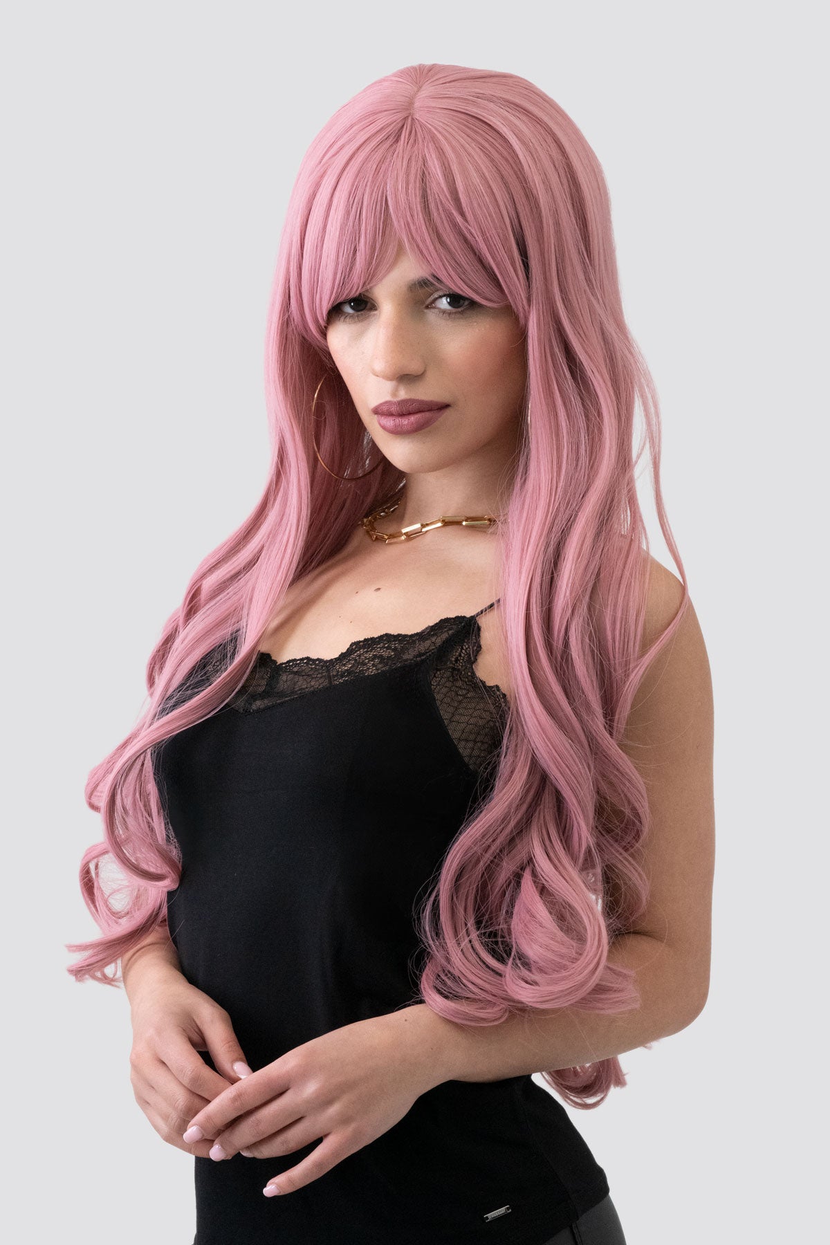 Woman with long pink wig wearing a black top on a white background. Long wavy pink wig with sweeping fringe: Millicent
