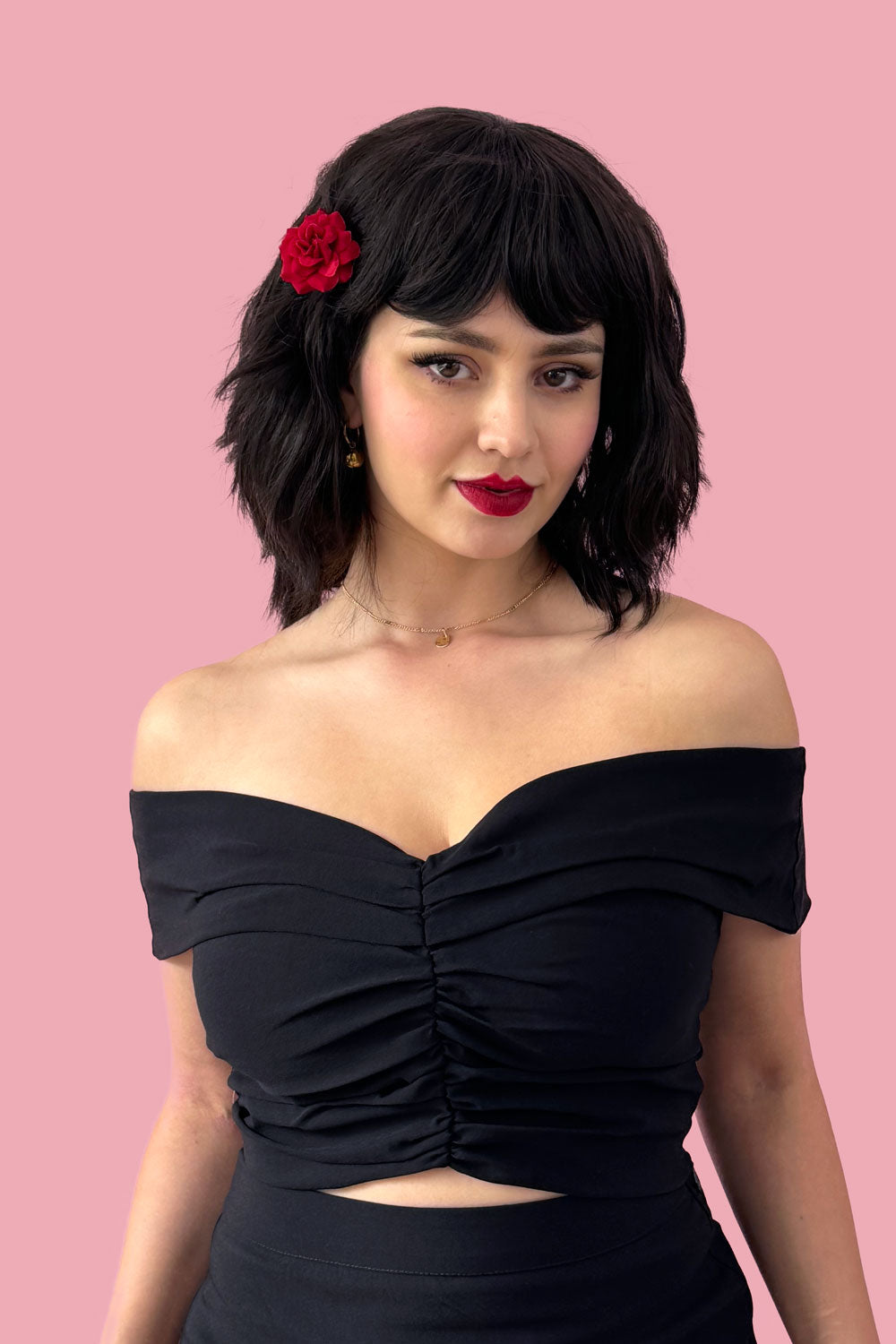 A person wearing a long dark brown bob wig with textured waves, styled with a fringe. The wig is shoulder-length, and the person is dressed in a black off-shoulder top against a pink background. Long dark brown bob wig (LOB) with textured waves: Anais