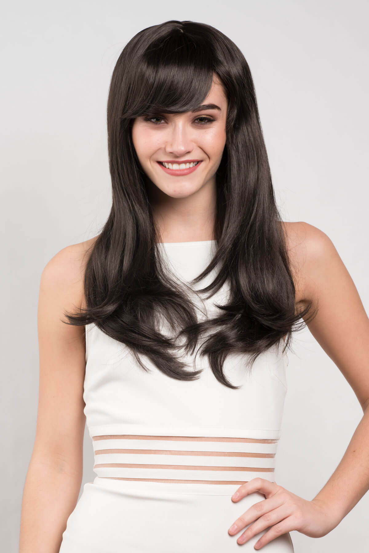 Woman with long dark hair wearing a white dress against a light gray background. Long dark brown wig, layered face frame style: Lucy