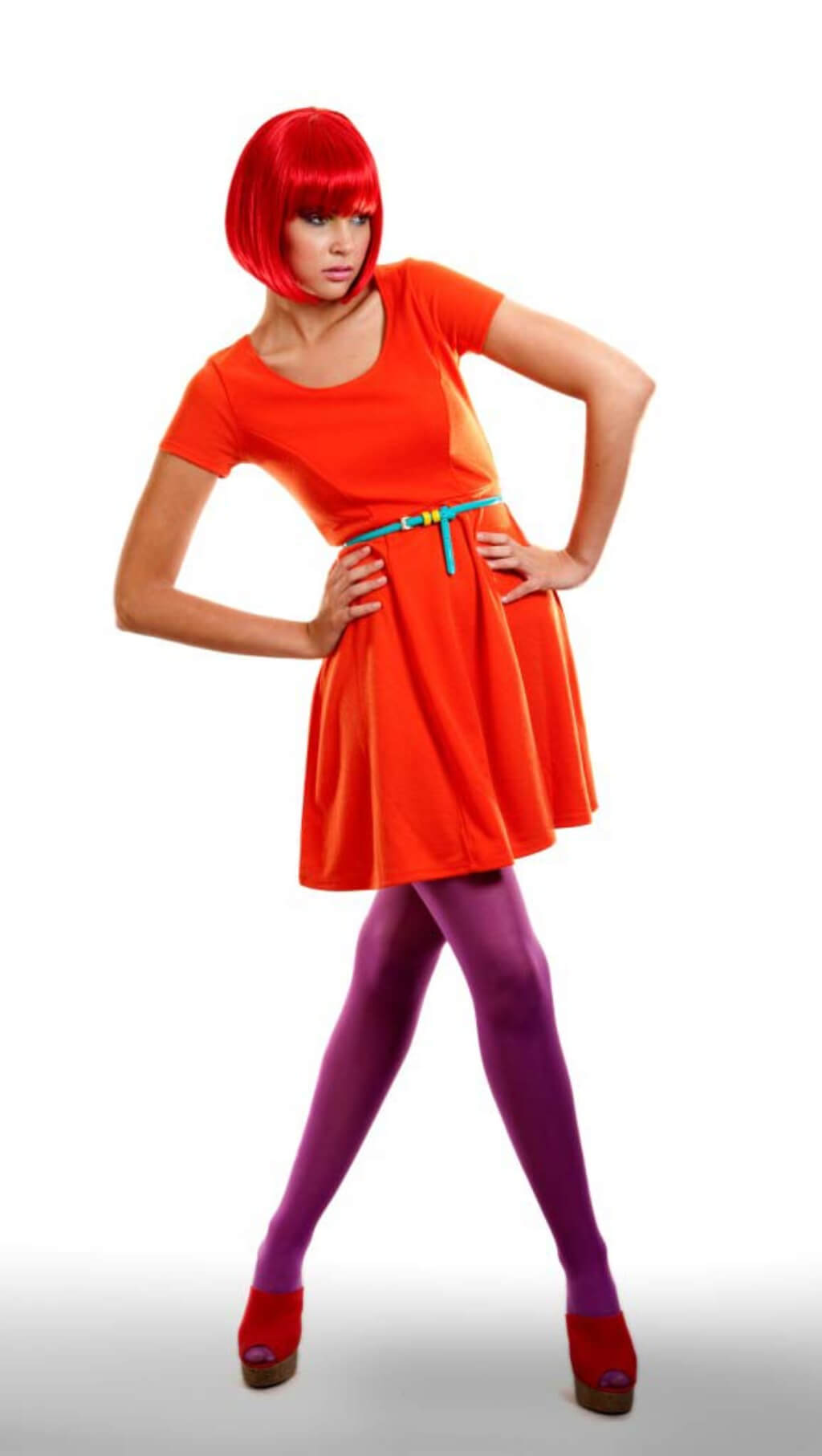 Person wearing a red wig and a bright orange dress with a colourful belt on a white background. Vibrant, bright red bob wig: Maisy