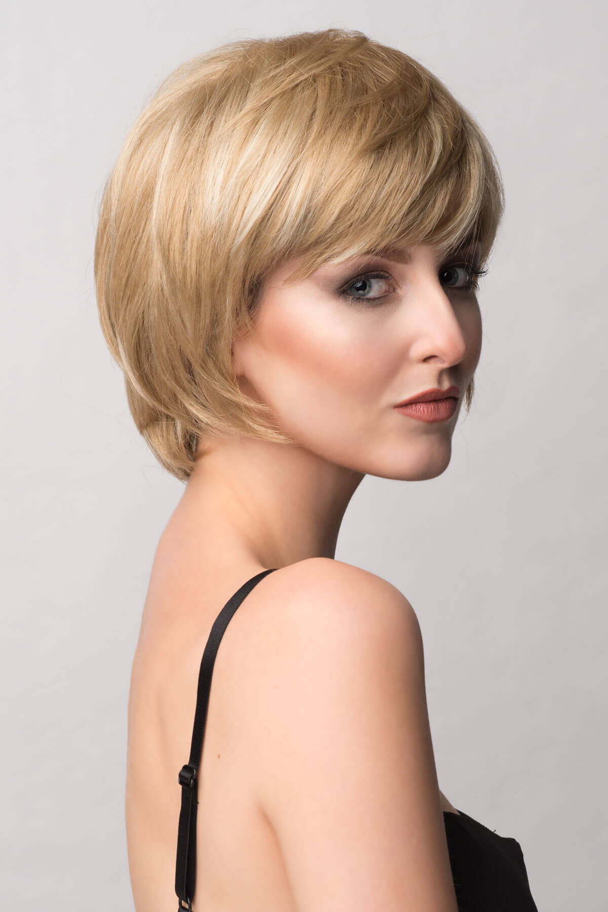 Woman with a stylish haircut against a plain background. Pixie cut wig, layered and short: Sophia