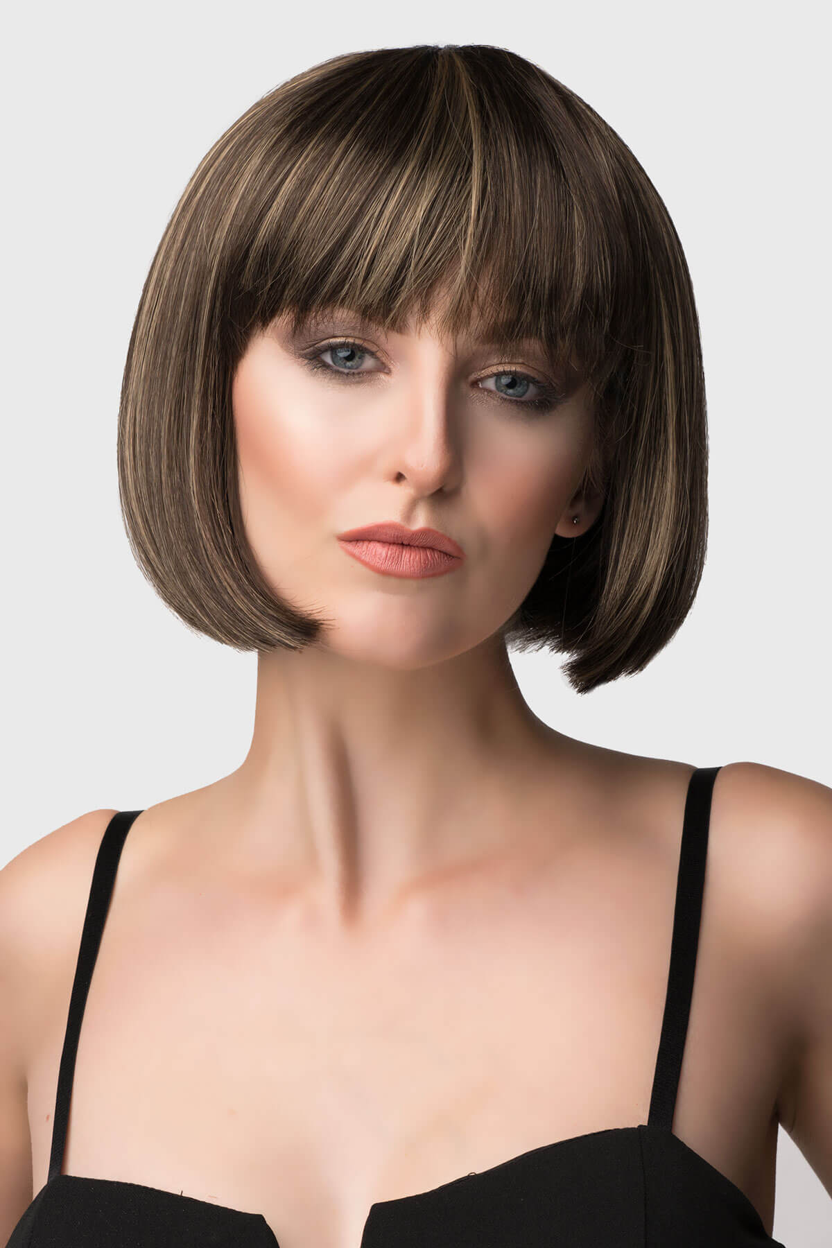 Woman with a stylish bob haircut and bangs against a plain background. Chestnut brown bob wig with blonde highlights: Lorna