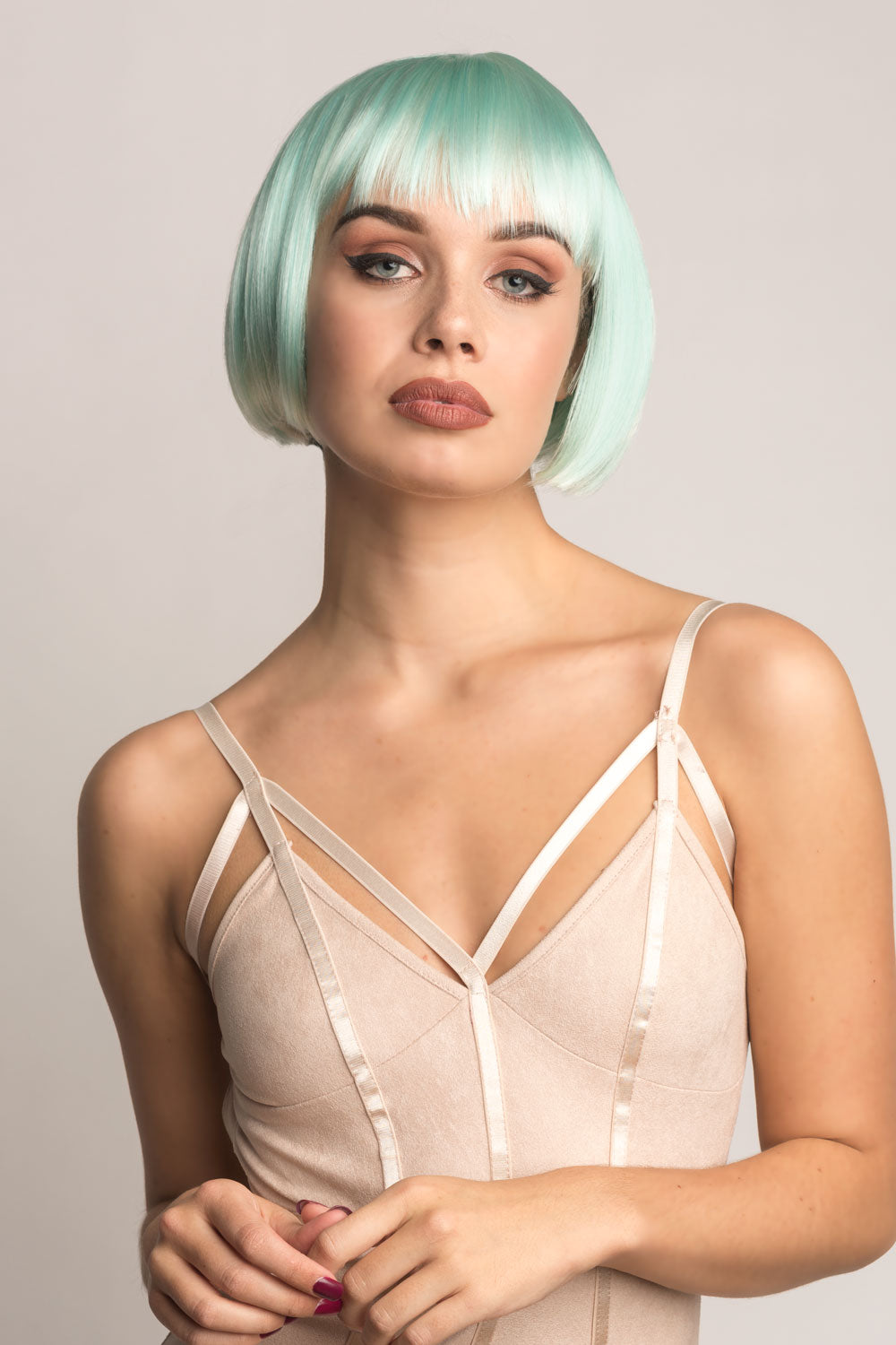 A person wearing a pale turquoise bob wig with washed out platinum tips, styled with a fringe that falls to the eyebrows and blunt cut layers. Turquoise bob wig, with platinum blonde ombre, short and chic: Eunice