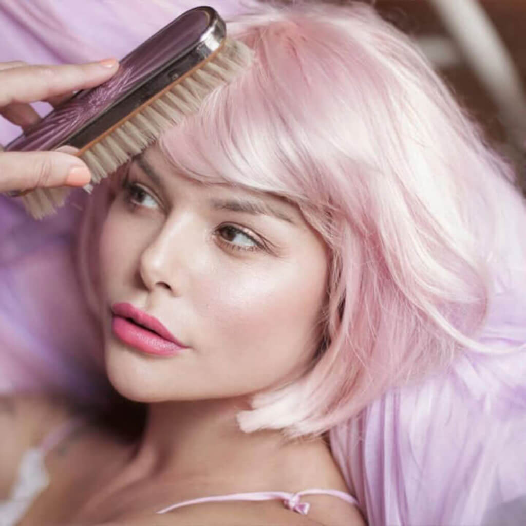 Woman with pink hair being combed by a brush, wearing a pink top. Louisa - Sleek, Blunt, Classic Ombre Pink and Platinum Bob Wig