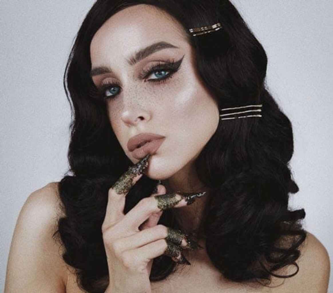 Woman with styled hair holding a decorative object against a plain background. Black soft glamour wig with long marcel waves: Vivienne