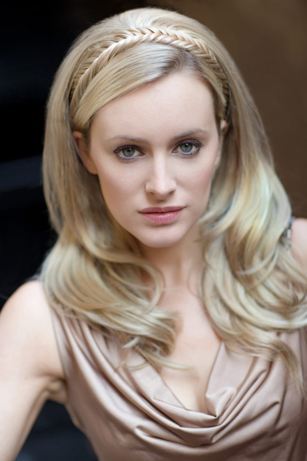 A woman wearing a fishtail plait hairband with a side braid, in a brown dress, with a neutral background. Fishtail plait hairband (braid)