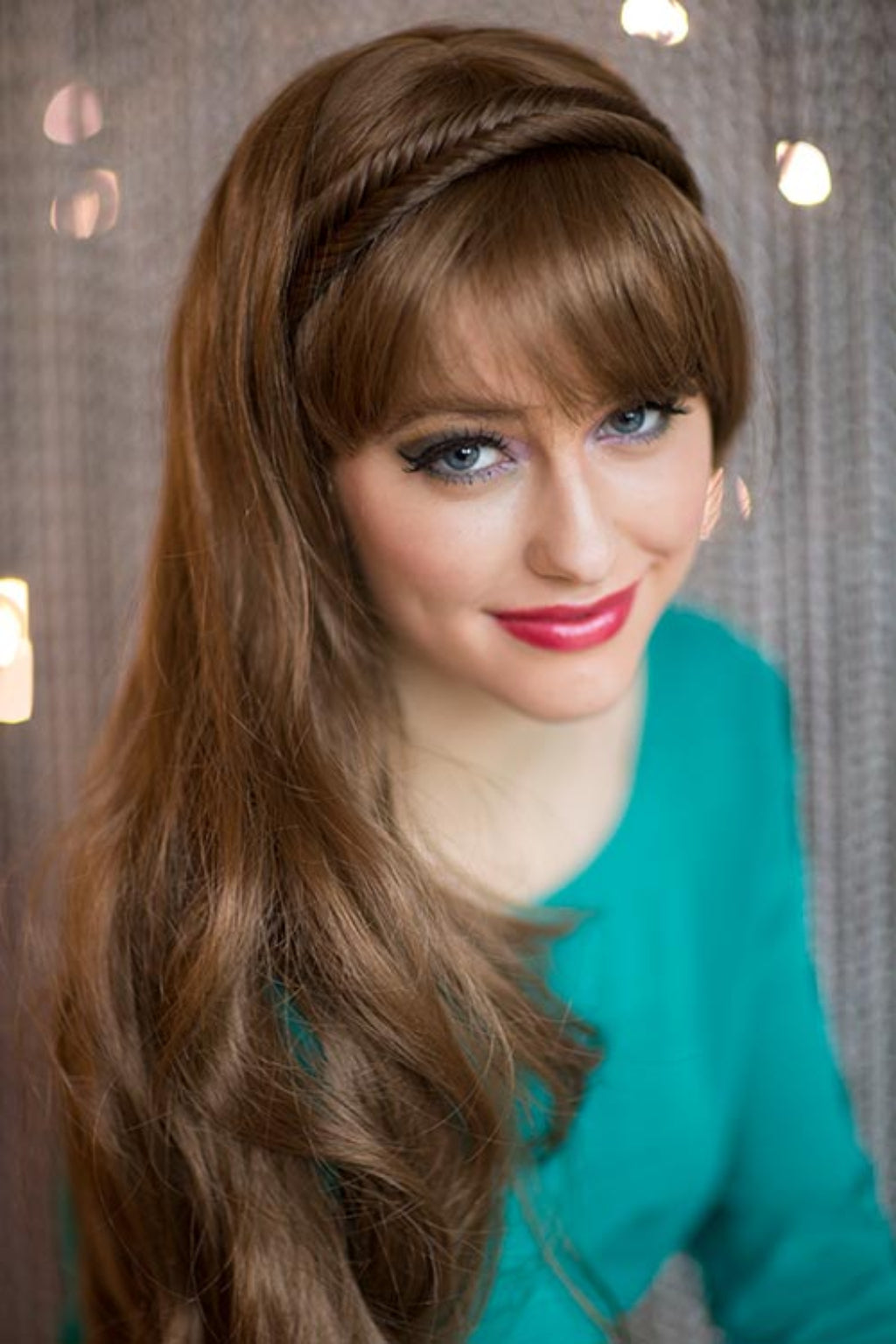 A woman wearing a fishtail plait hairband with a side braid, in a brown dress, with a neutral background.